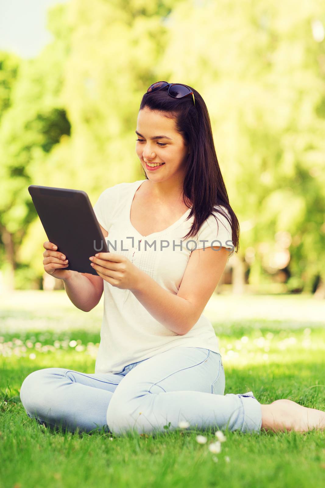 smiling young girl with tablet pc sitting on grass by dolgachov