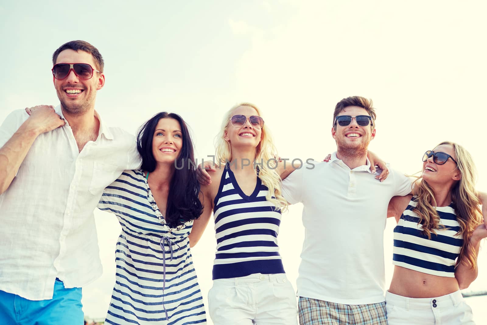 smiling friends in sunglasses walking on beach by dolgachov