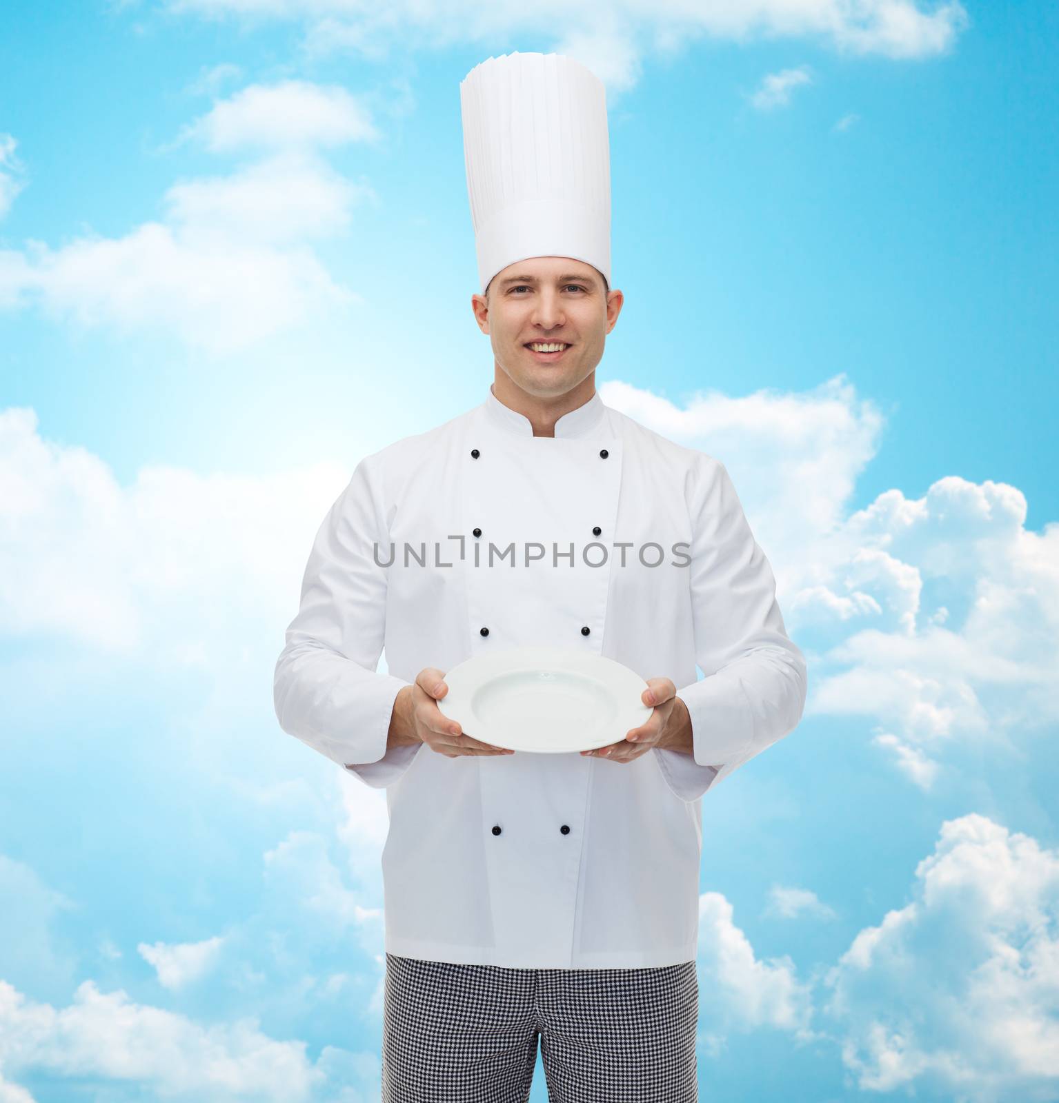 cooking, profession, advertisement and people concept - happy male chef cook showing something on empty plate over blue sky with clouds background