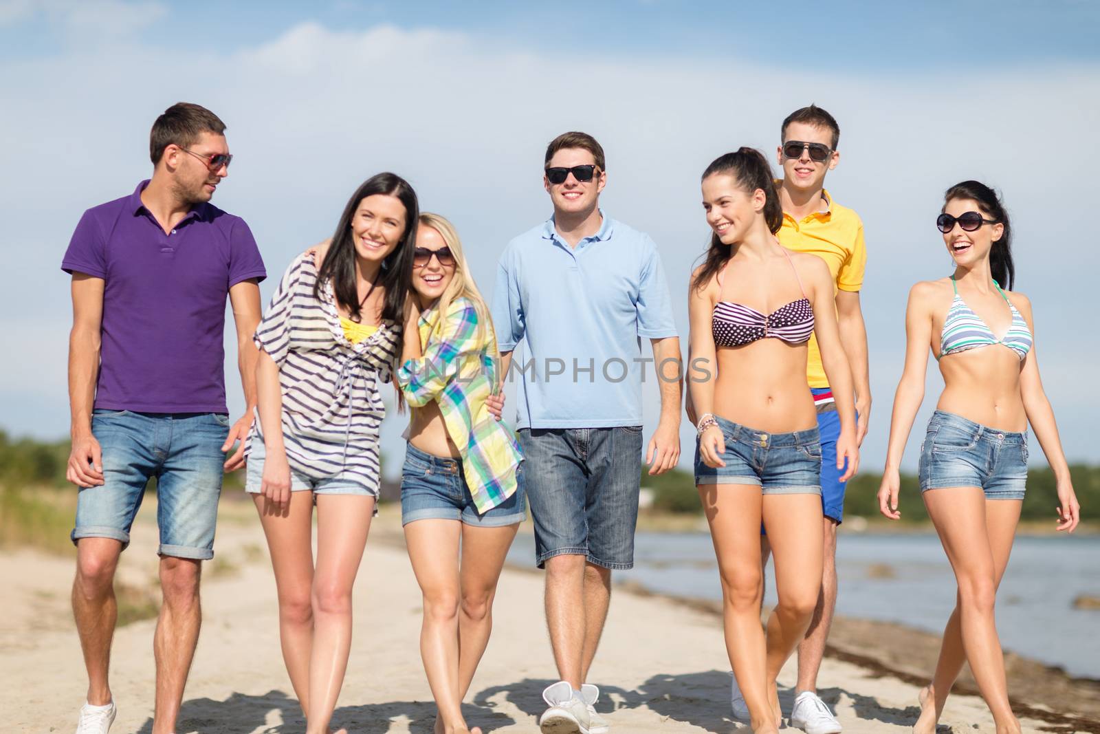 group of happy friends walking along beach by dolgachov