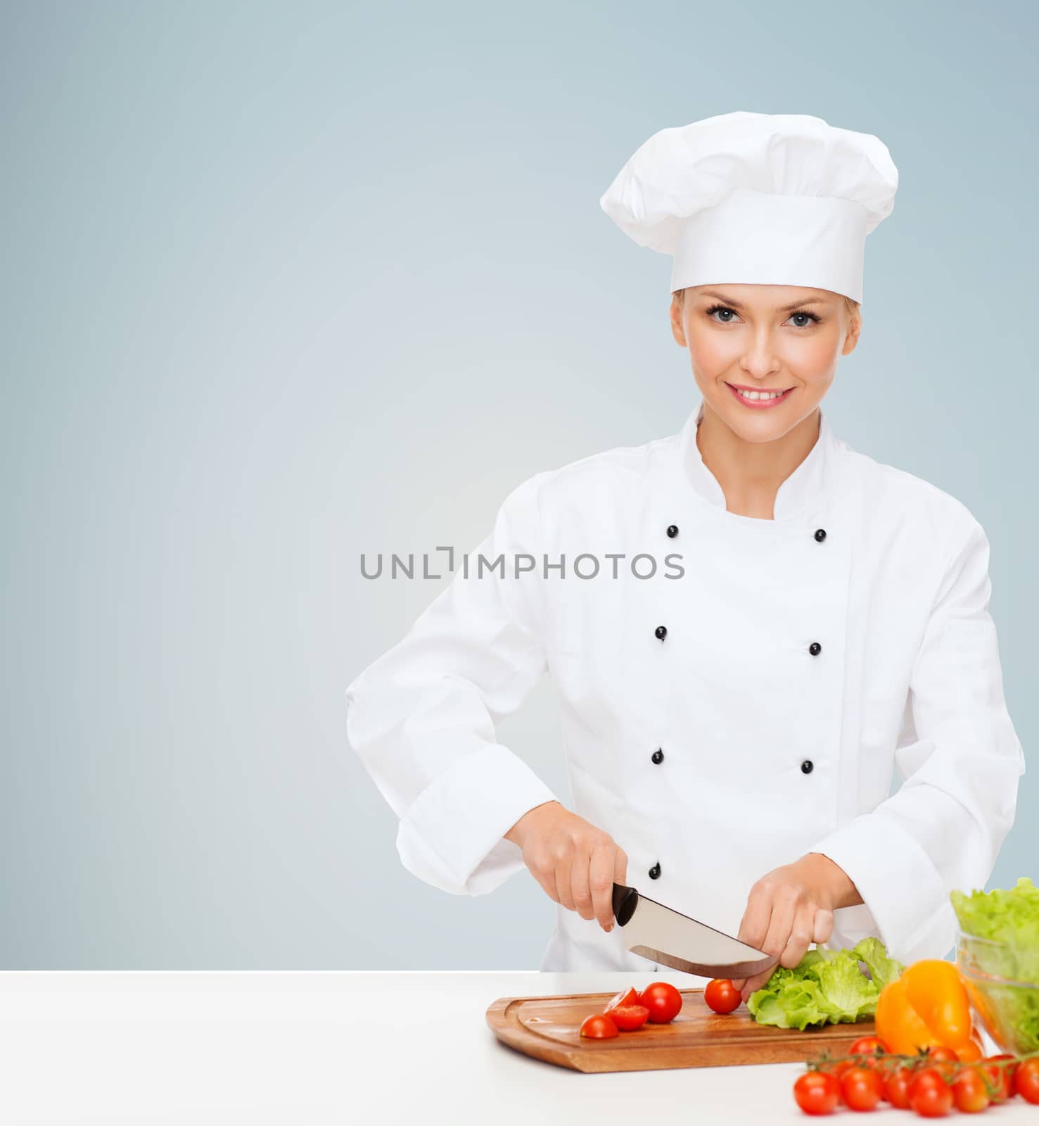 cooking and food concept - smiling female chef, cook or baker chopping vegetables over gray background