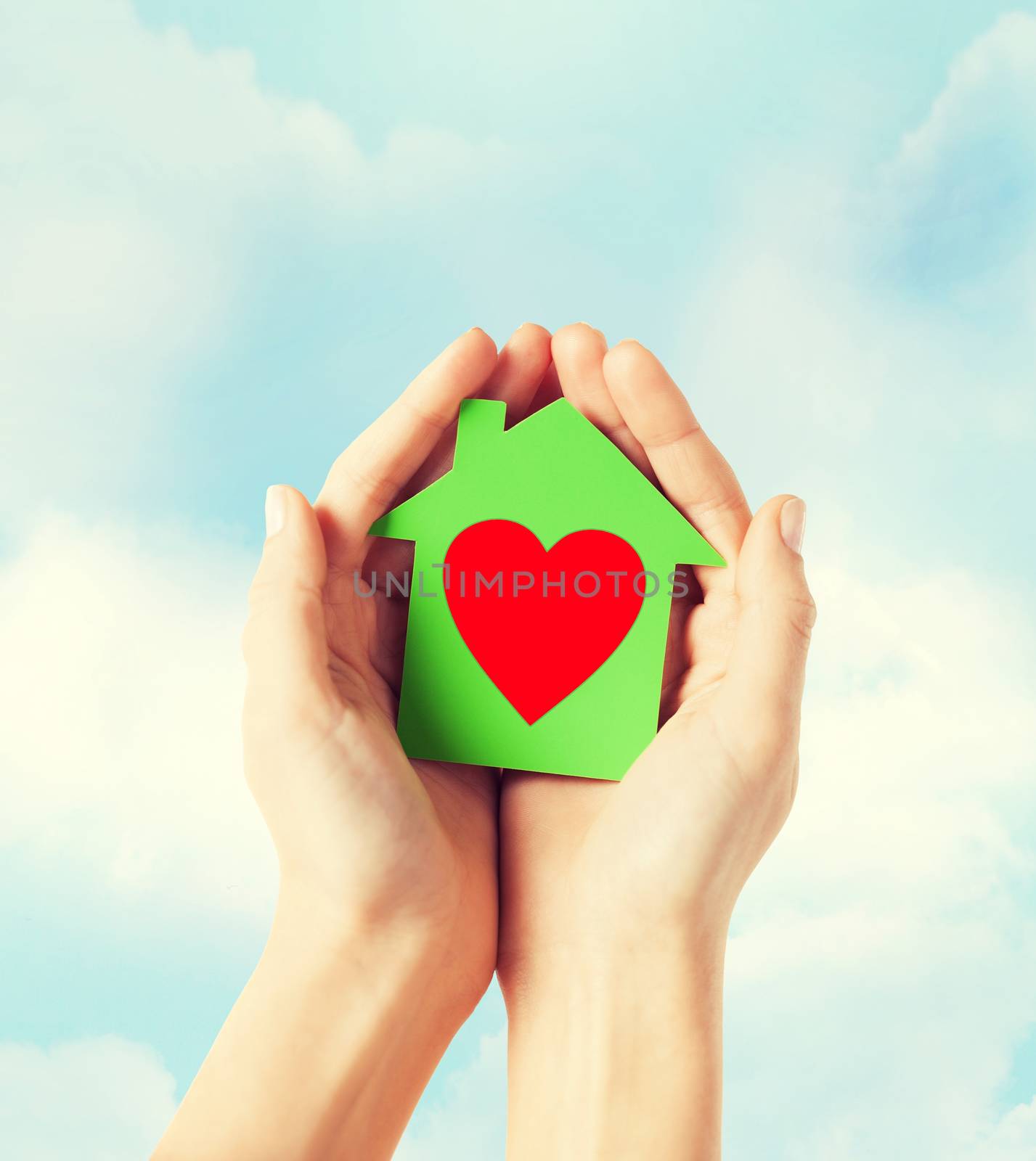 charity, real estate and family home concept - closeup picture of female hands holding green paper house with red heart