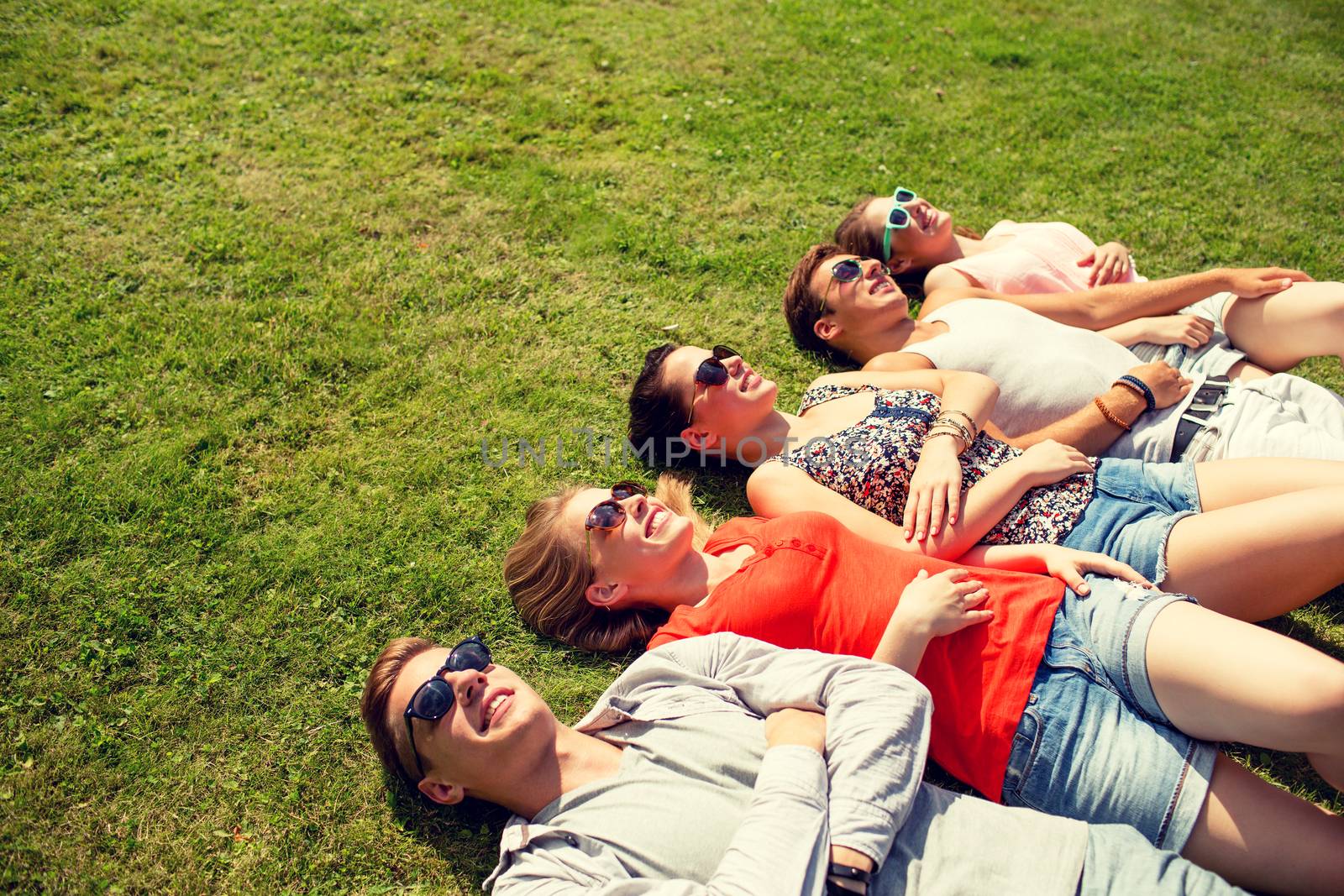 group of smiling friends lying on grass outdoors by dolgachov