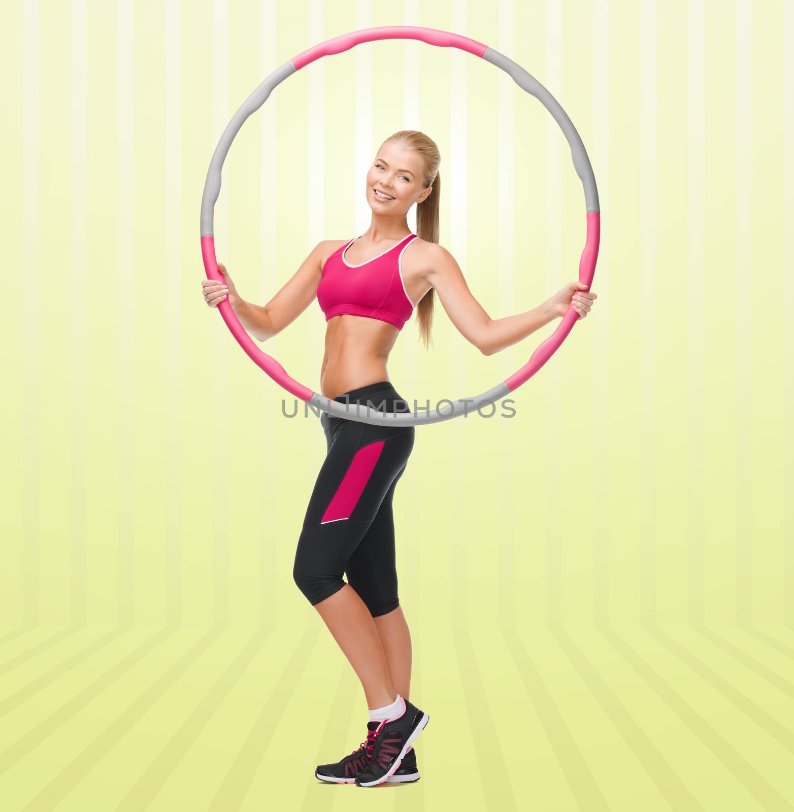 fitness, sport, people and healthcare concept - young sporty woman exercising with hula hoop over yellow striped background