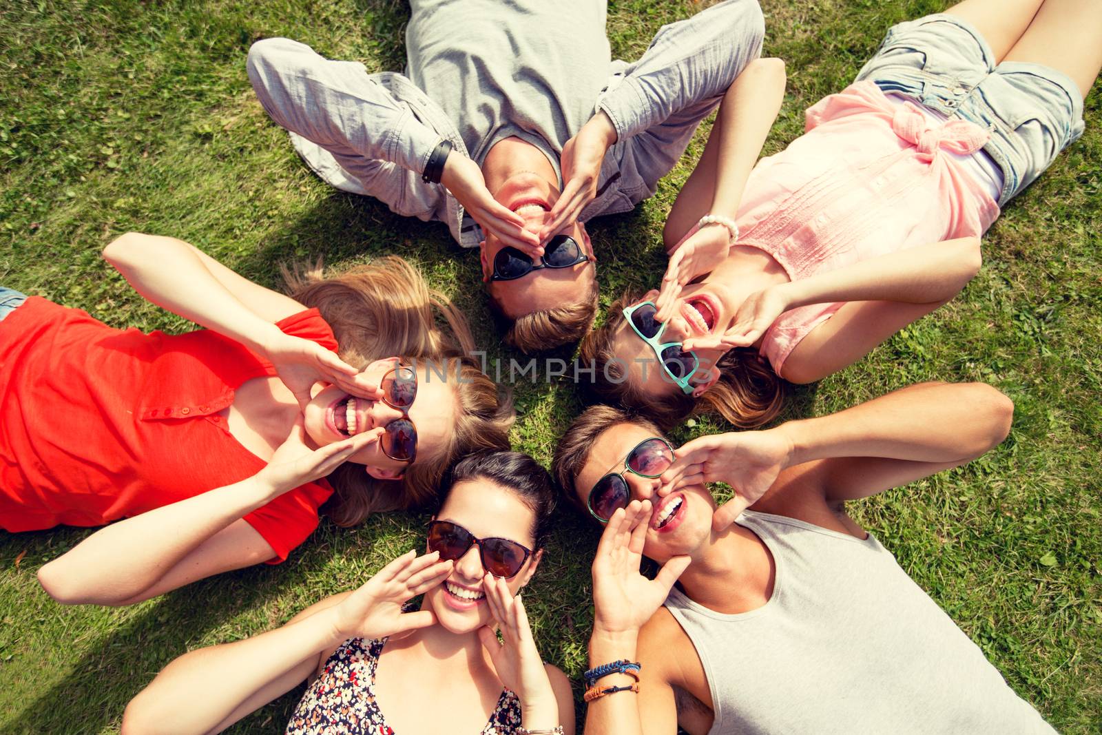 group of smiling friends lying on grass outdoors by dolgachov