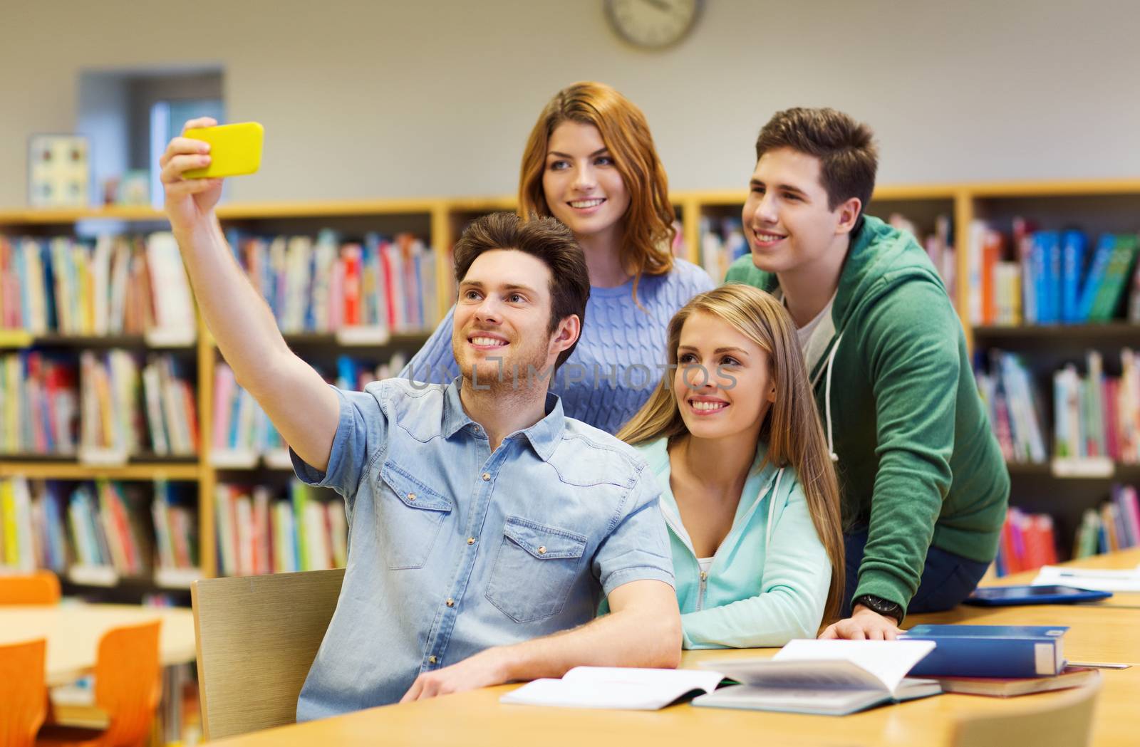 people, technology, friendship, education and school concept - group of happy students with smartphone taking selfie at library