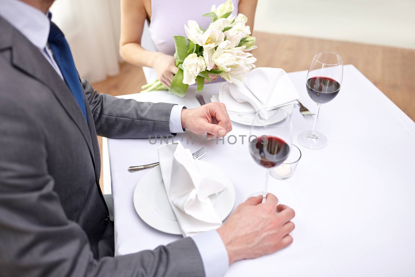 restaurant, people, celebration and holiday concept - close up of young couple with tulip flowers and glasses of red wine at restaurant