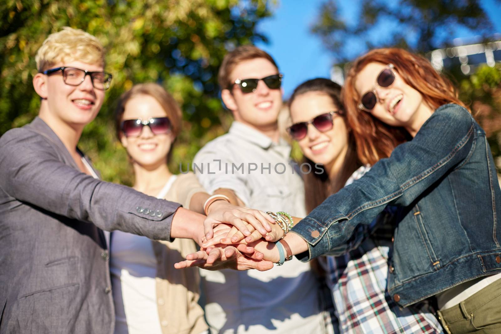 friendship, togetherness, team and people concept - close up of teenage friends in sunglasses with hands on top