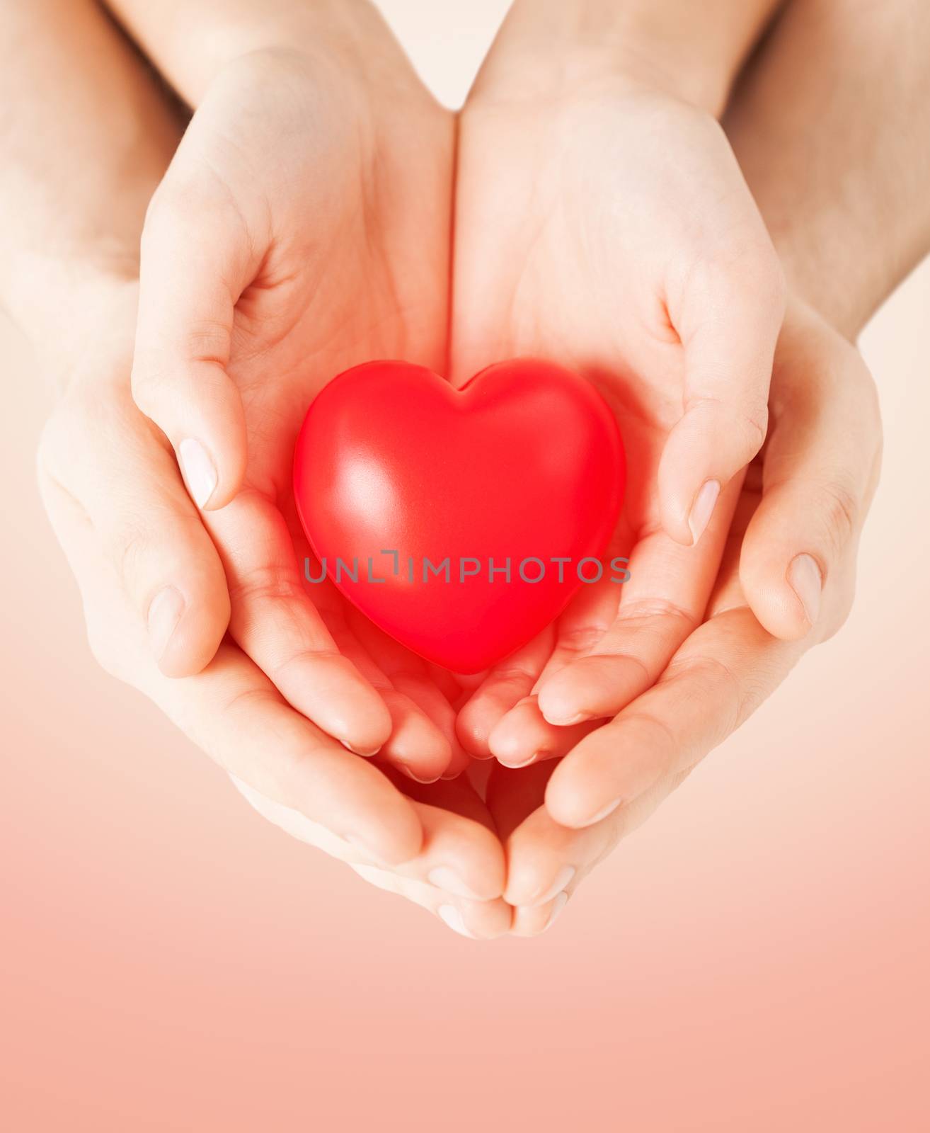 health, love and relationships concept - close up of couple hands with big red heart over beige background