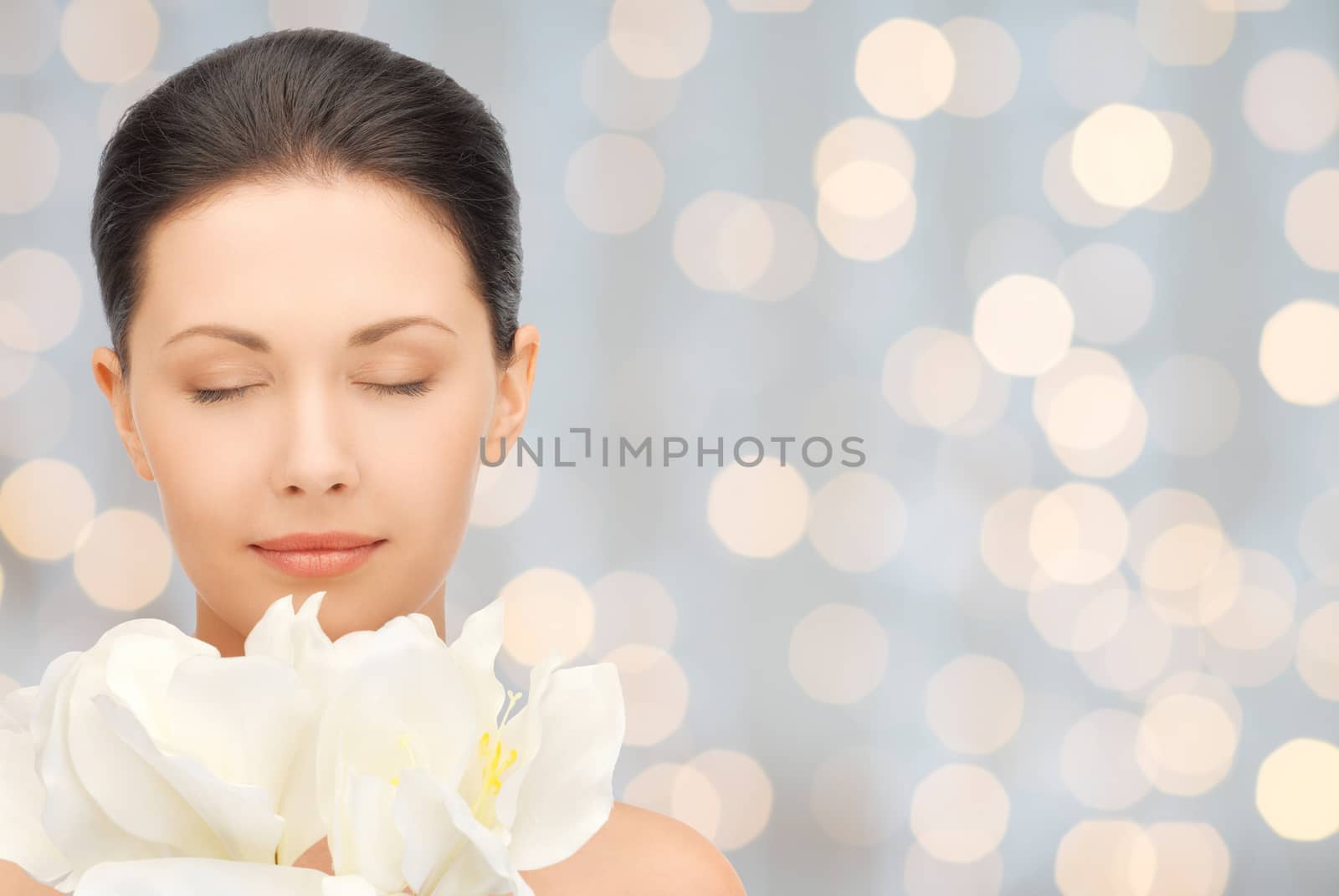 beauty, people, holidays and health concept - beautiful young woman smelling flowers with closed eyes over lights background