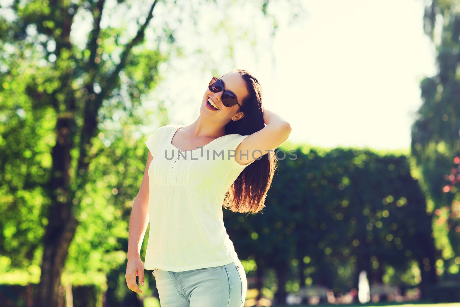 summer, leisure, vacation and people concept - smiling young woman wearing sunglasses standing in park