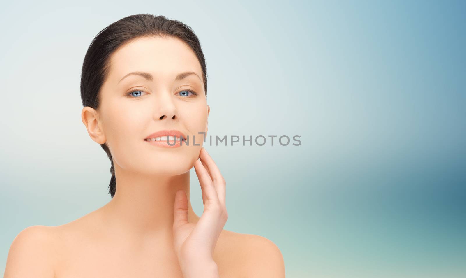 beauty, people and health concept - beautiful young woman touching her face over blue background