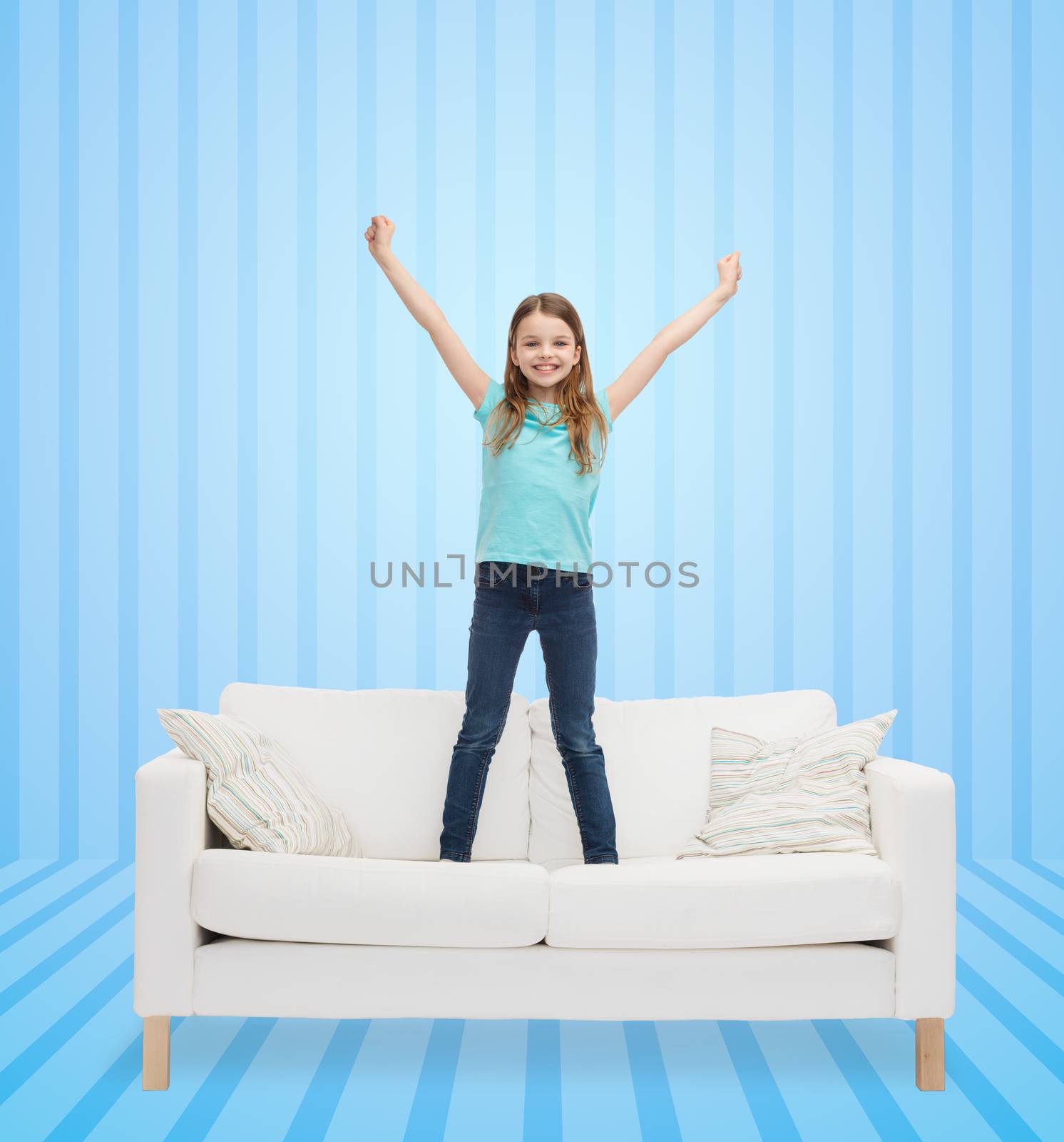 home, leisure, people and happiness concept - smiling little girl jumping on sofa over blue striped background