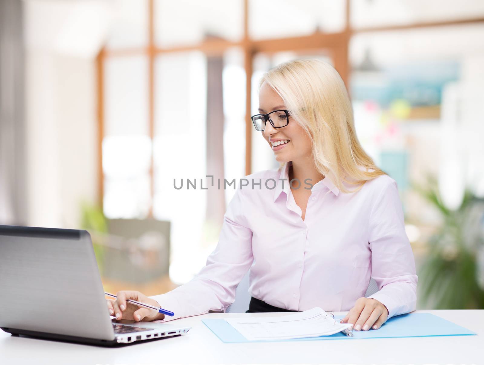 education, business and technology concept - smiling businesswoman or student in eyeglasses with laptop computer and documents over office room background