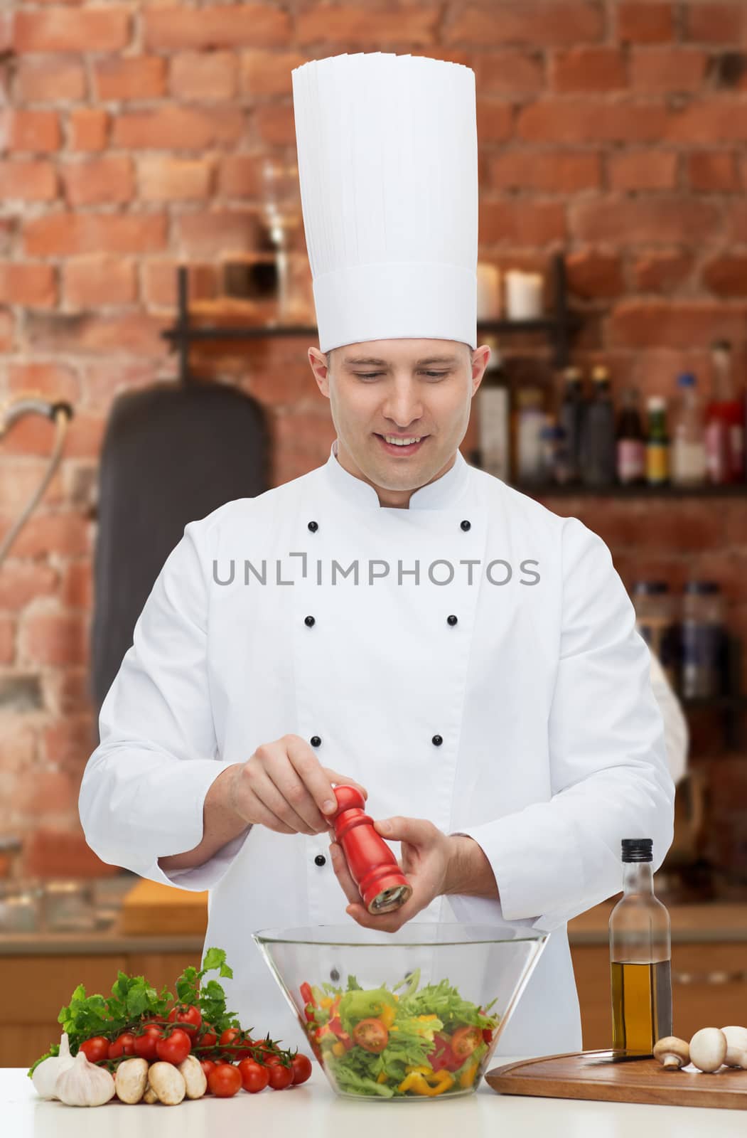 profession, vegetarian, food and people concept - happy male chef cooking and seasoning vegetable salad over kitchen background