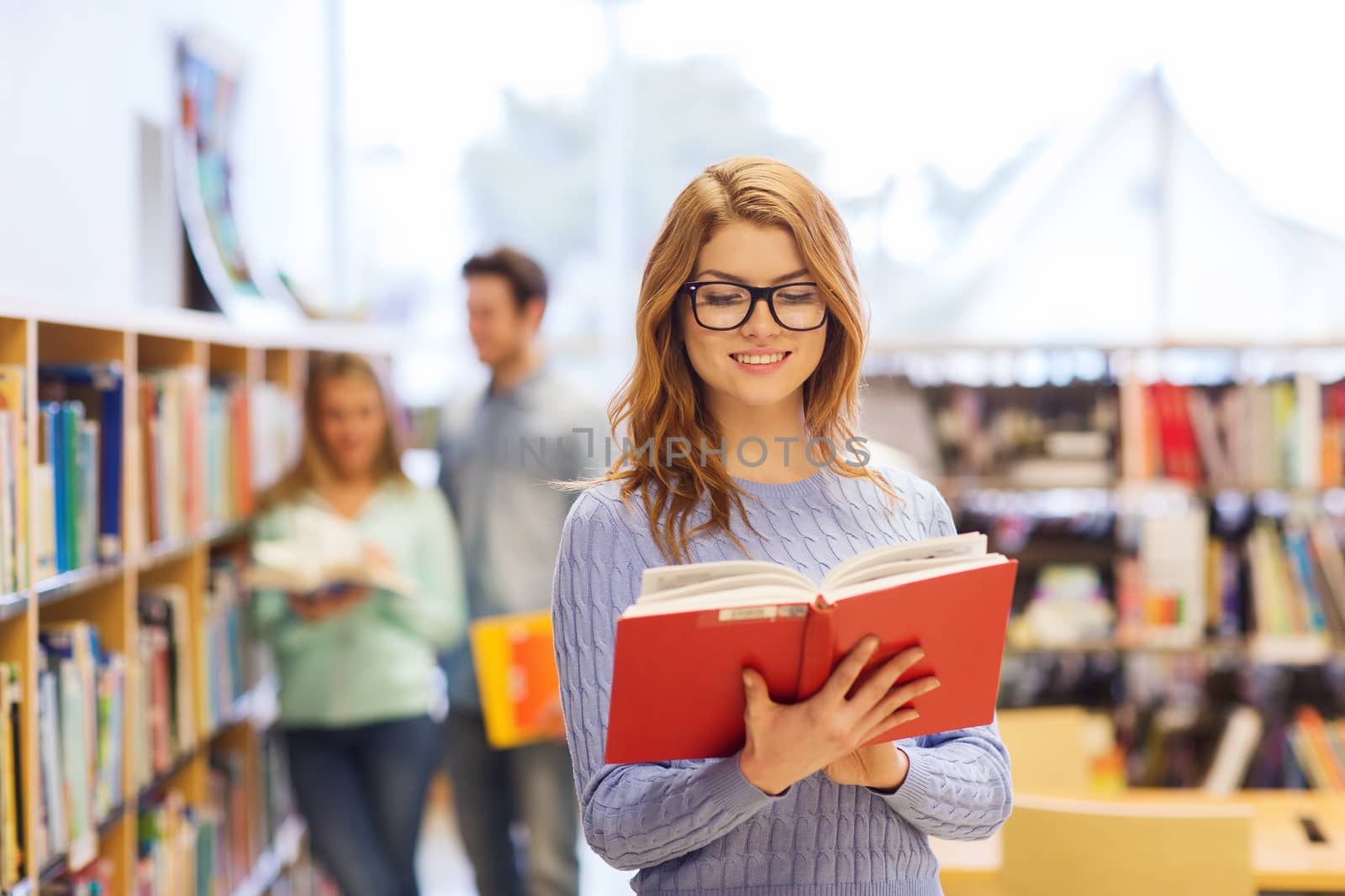 people, knowledge, education and school concept - happy student girl or young woman with book in library
