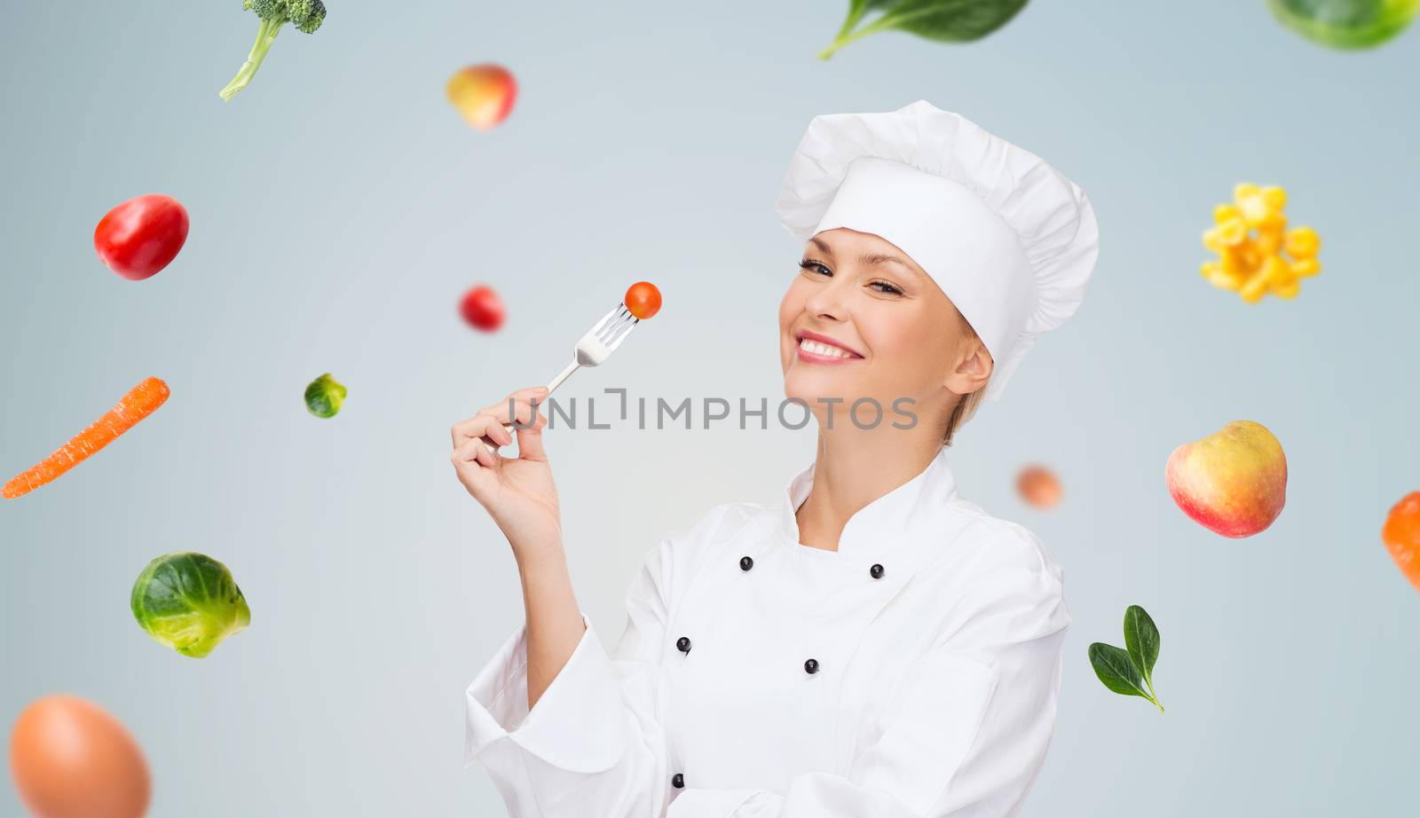 cooking and food concept - smiling female chef, cook or baker with fork and tomato over falling vegetables on gray background