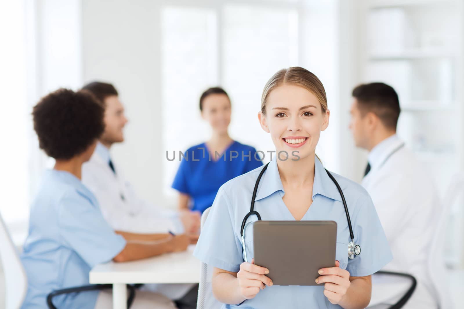 clinic, profession, people and medicine concept - happy female doctor with tablet pc computer over group of medics meeting at hospital