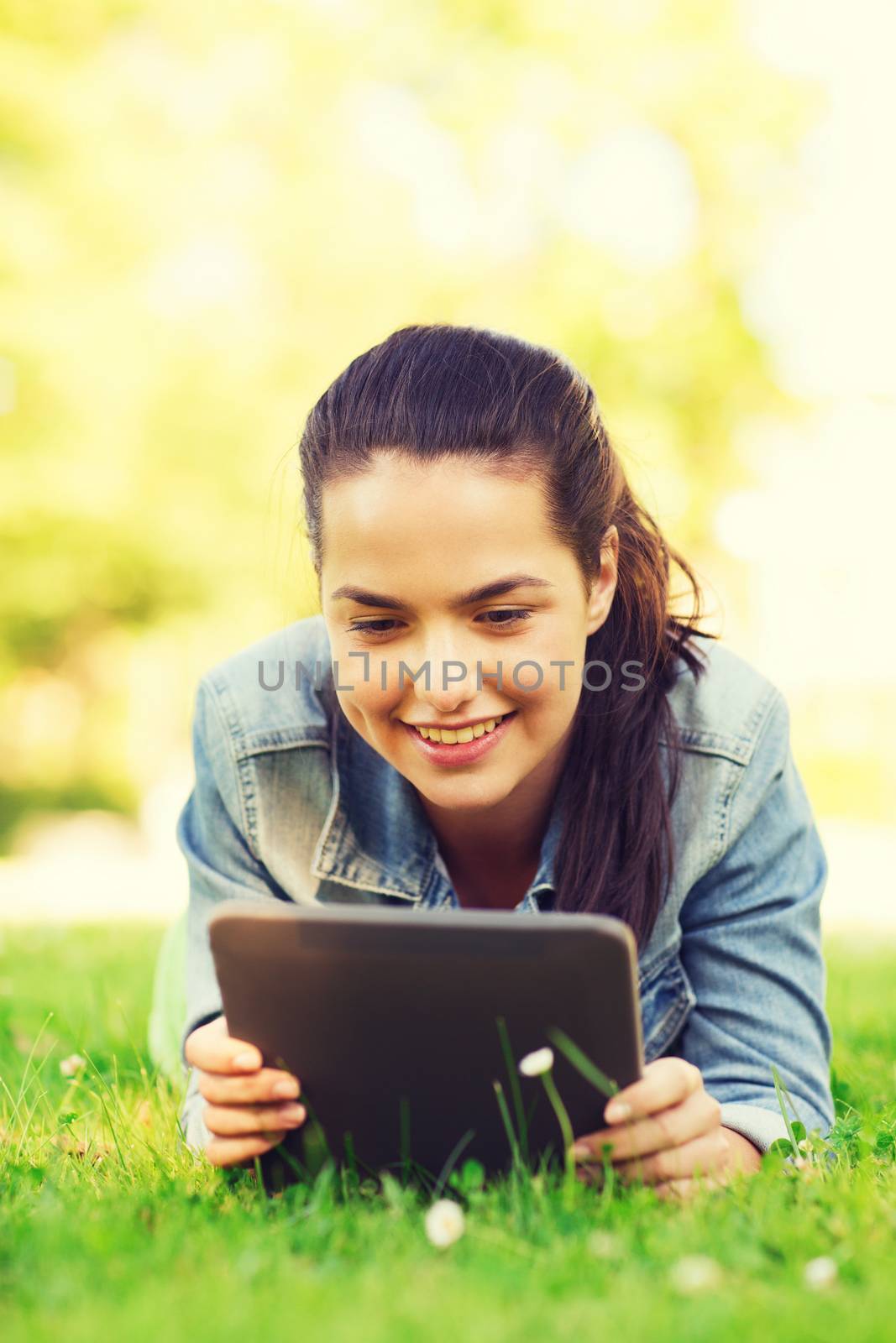 lifestyle, summer vacation, technology, leisure and people concept - smiling young girl with tablet pc computer lying on grass in park