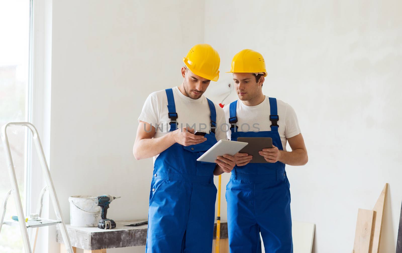 building, renovation, technology, electricity and people concept - two builders with tablet pc computer and smartphone indoors