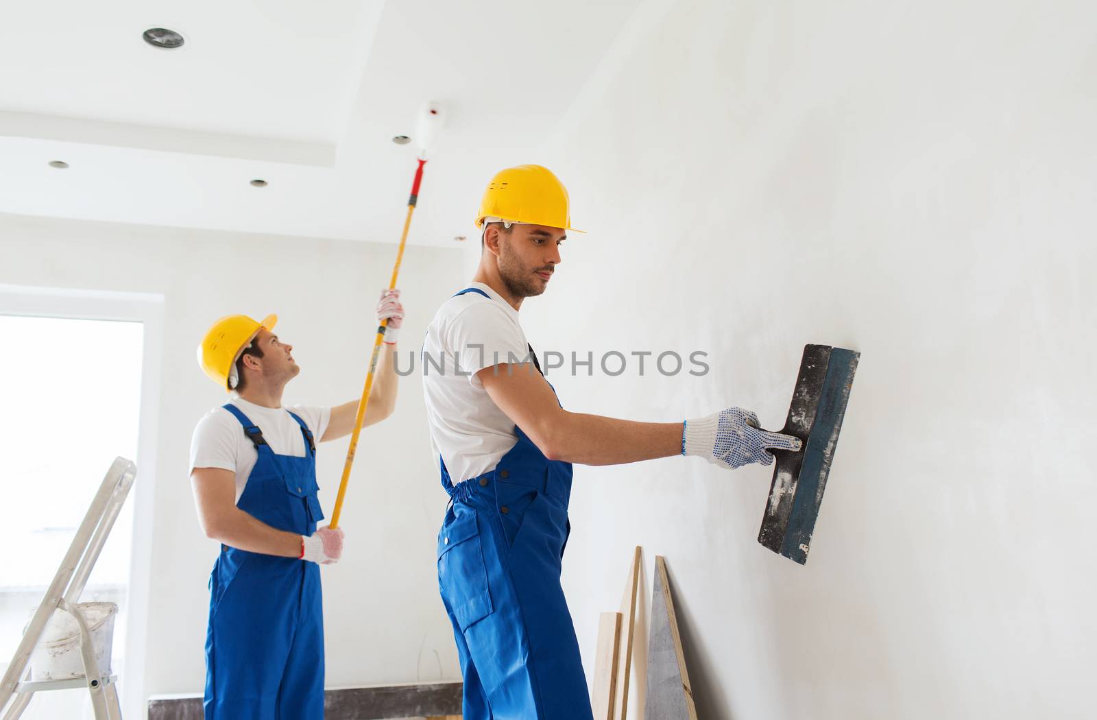 business, building, teamwork and people concept - group of builders in hardhats with plastering tools indoors