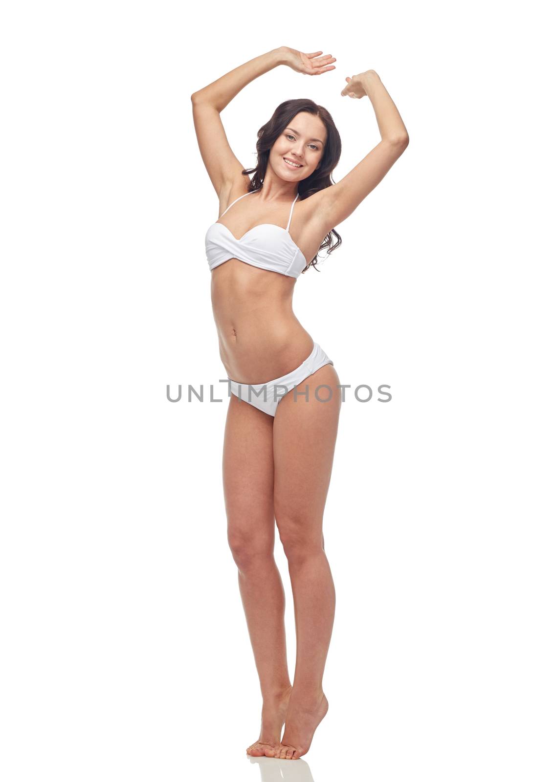 people, fashion, swimwear, summer and beach concept - happy young woman posing in white bikini swimsuit with raised hands