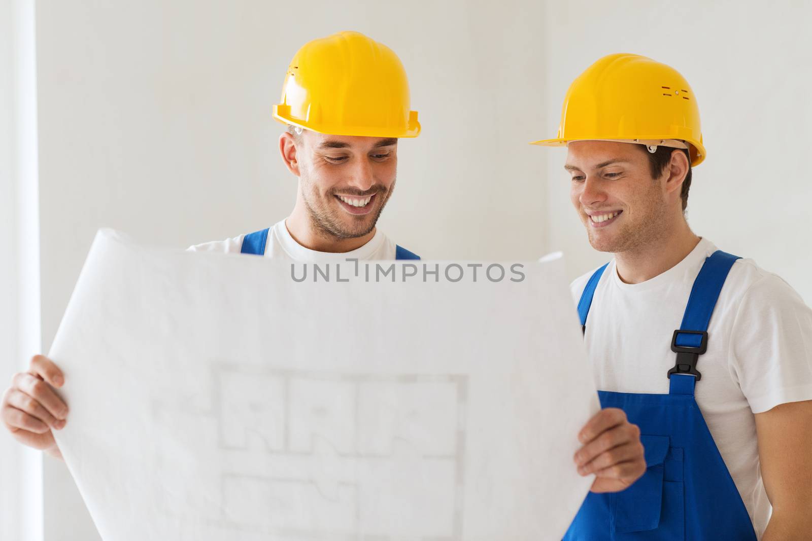 building, teamwork and people concept - group of smiling builders in hardhats with blueprint indoors