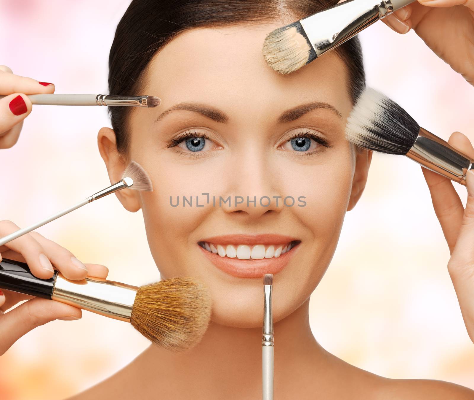 beauty, people and makeup concept - closeup of beautiful woman getting professional make-up with many brushes over beige background