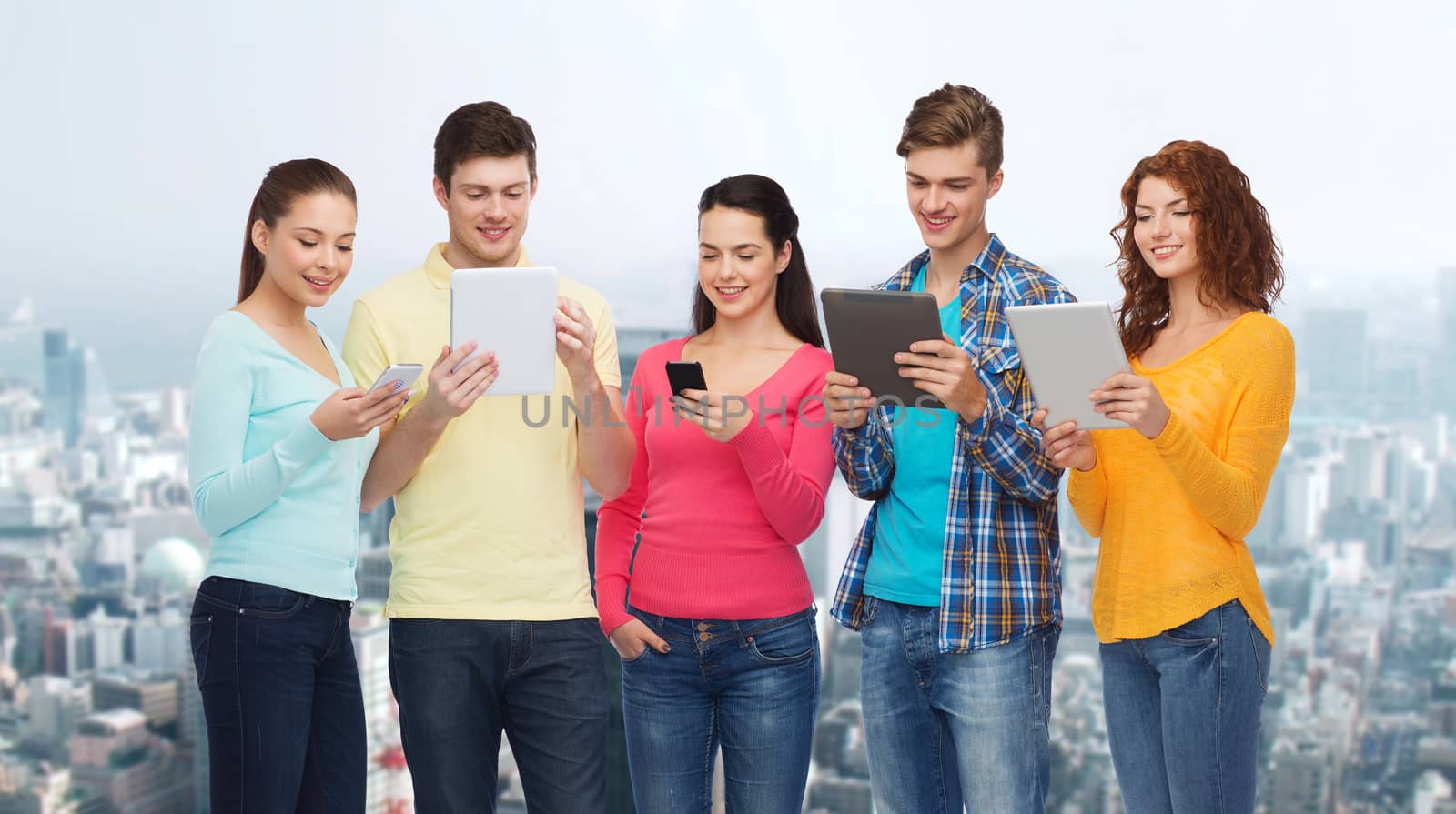 friendship, technology and people concept - group of smiling teenagers with smartphones and tablet pc computers over city background