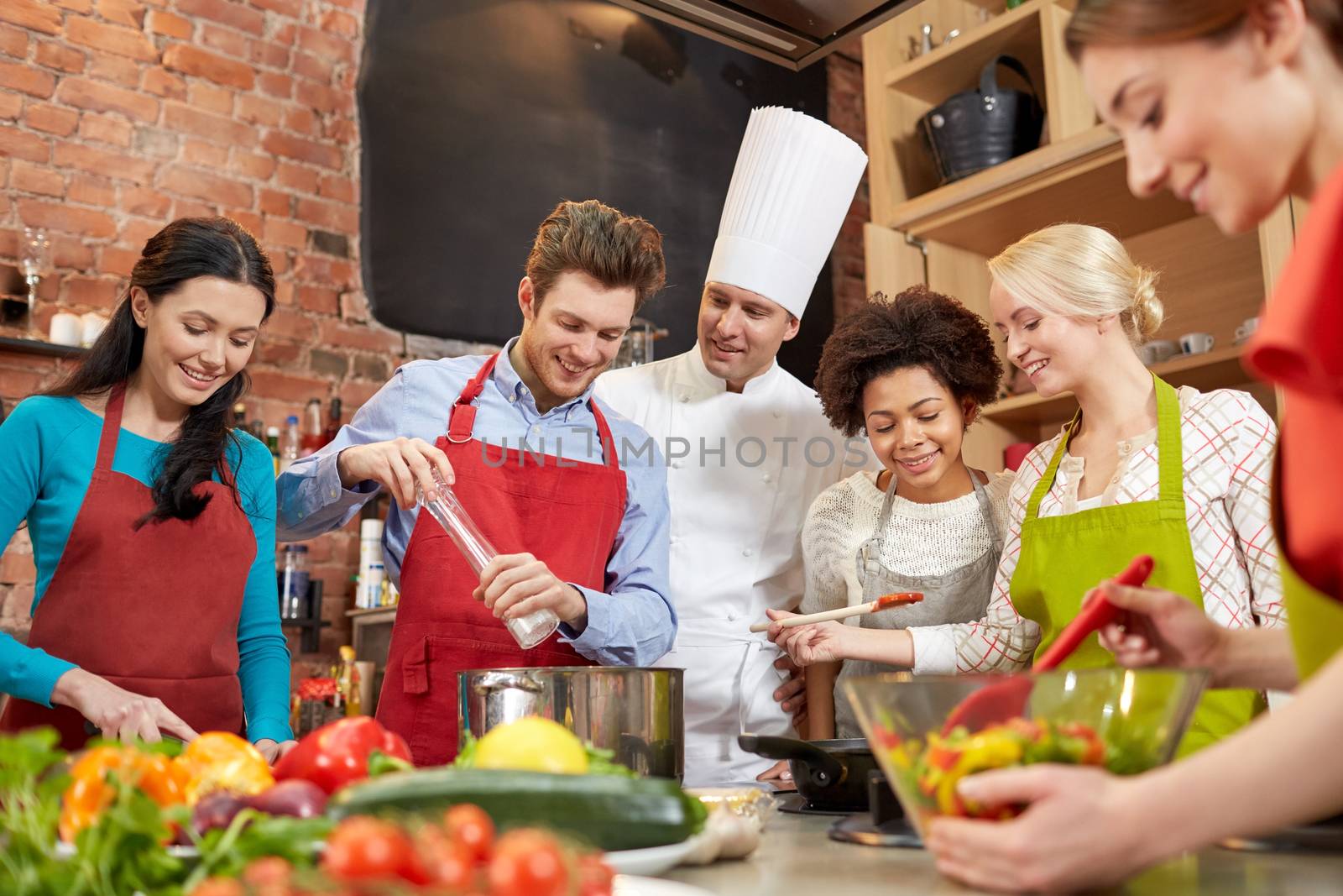 cooking class, culinary, food and people concept - happy group of friends and male chef cook cooking in kitchen