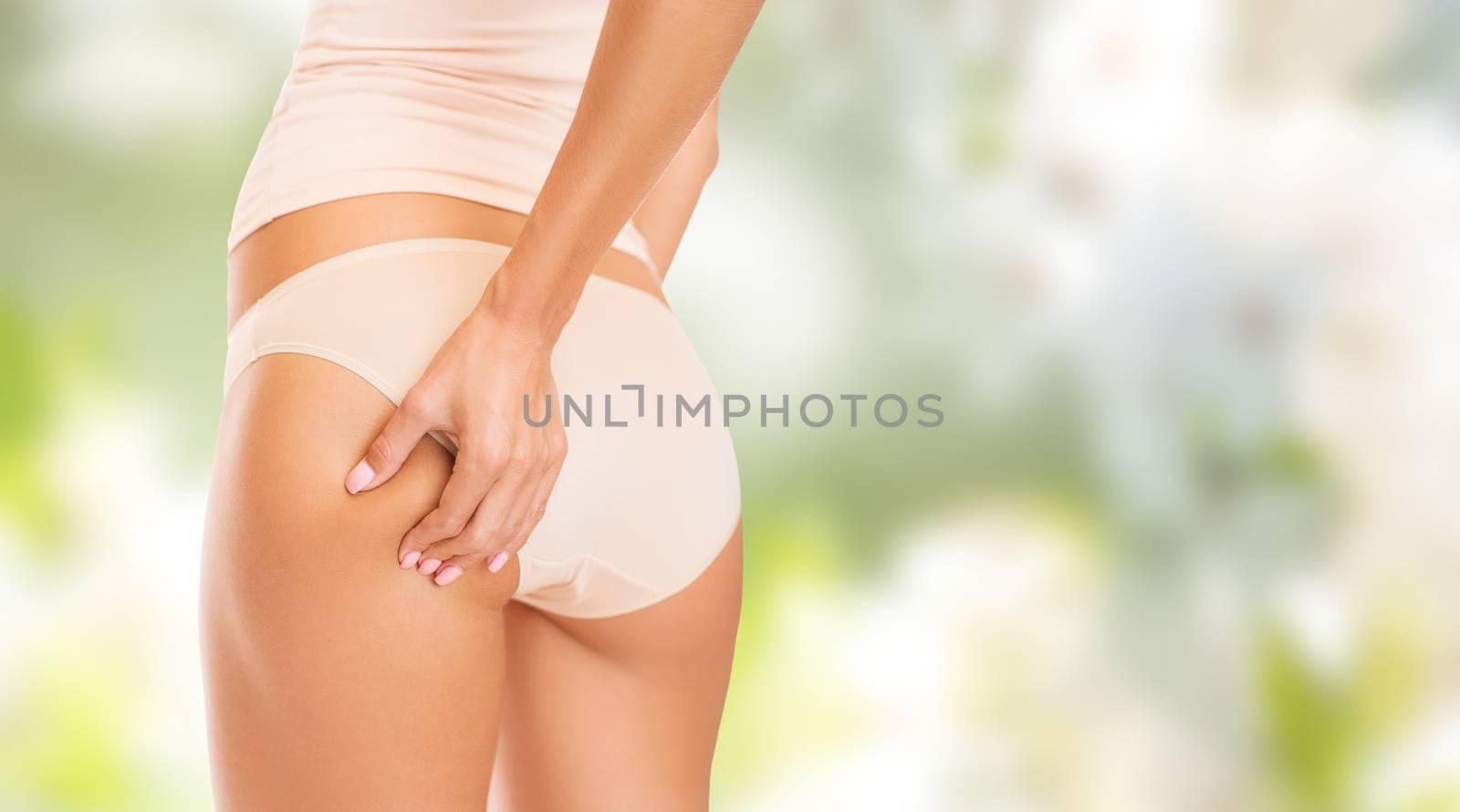 people, health, body care and beauty concept - close up of woman in underwear touching buttock over green background