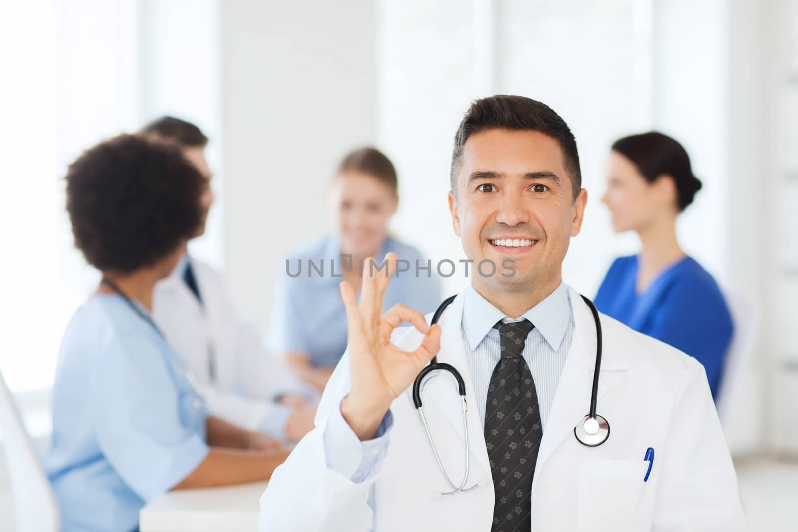 clinic, profession, people and medicine concept - happy male doctor over group of medics meeting at hospital showing ok hand sign