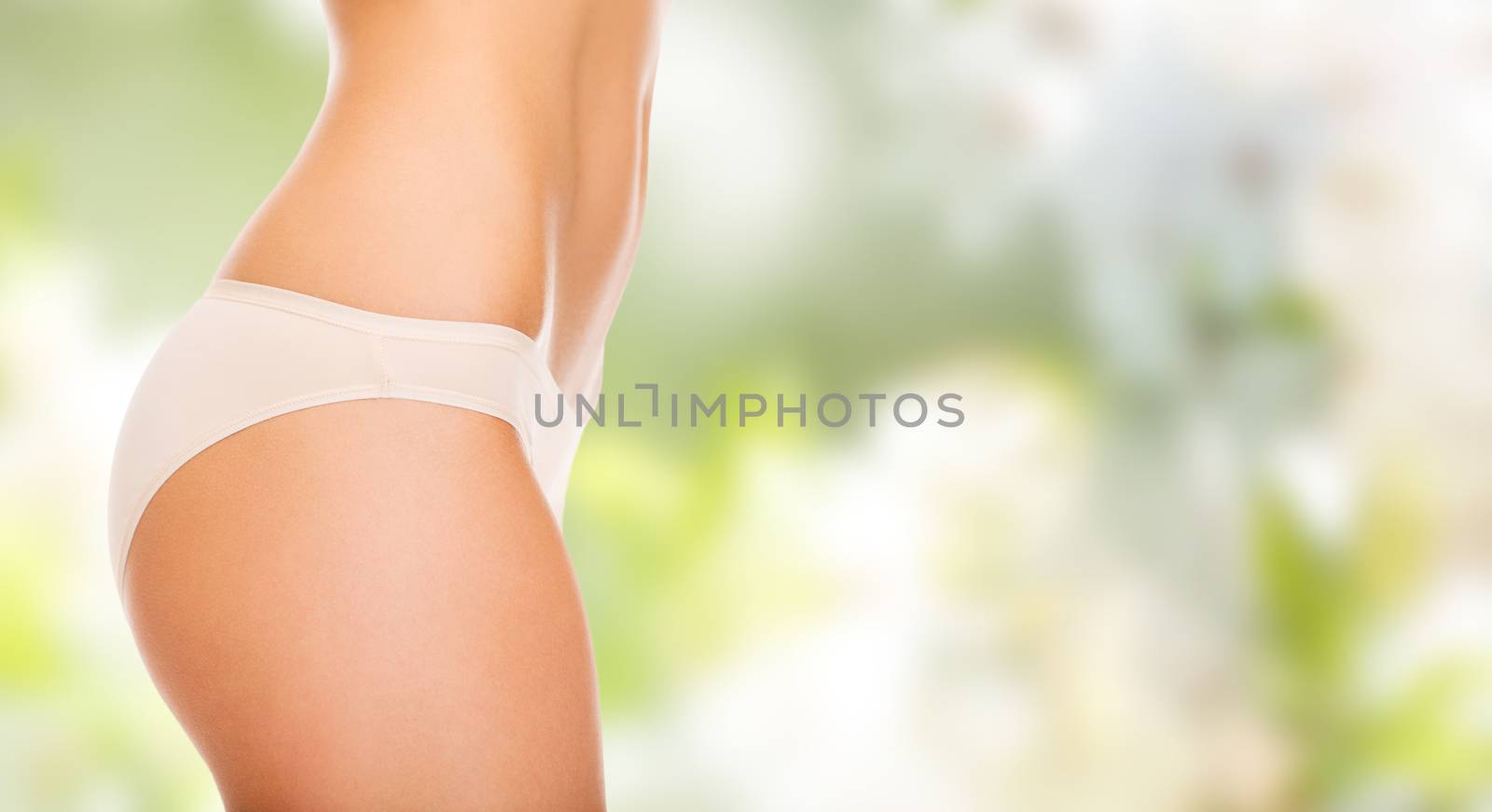 people, health, body care and beauty concept - close up of slim woman tummy and hips in underwear over green background