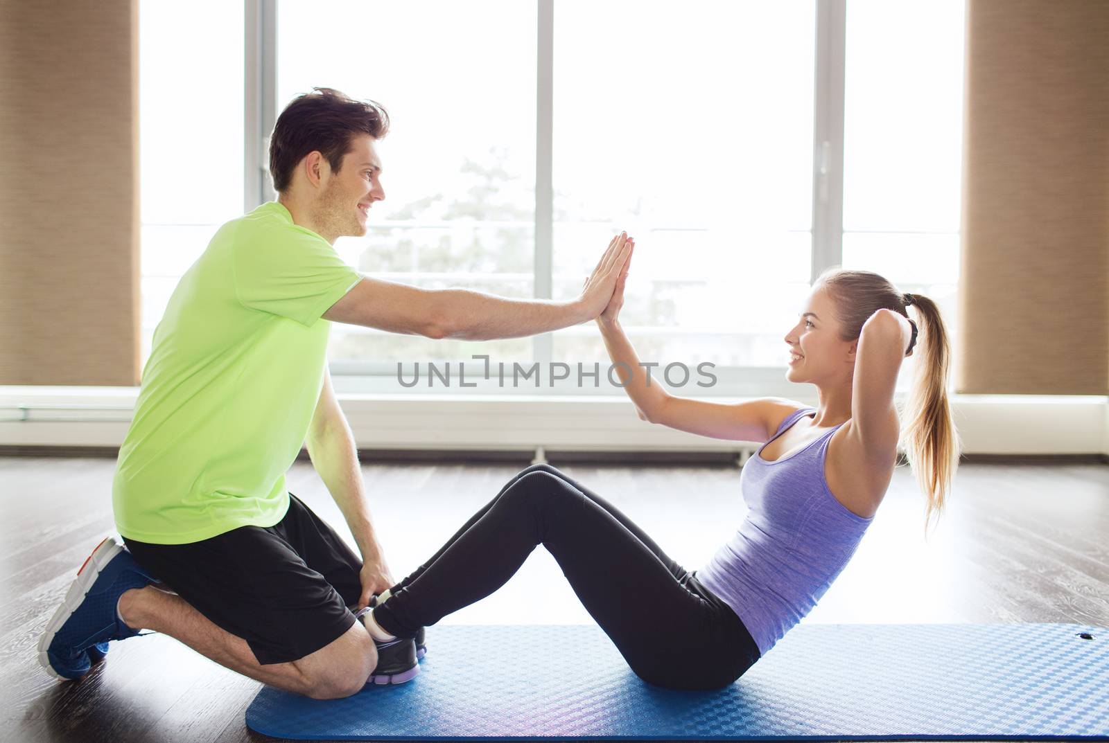 fitness, sport, training, teamwork and people concept - happy woman with personal trainer doing sit ups and high five gesture in gym