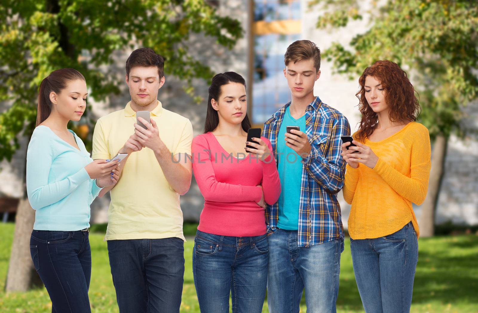 friendship, technology, education, school and people concept - group of serious teenagers with smartphones over campus background