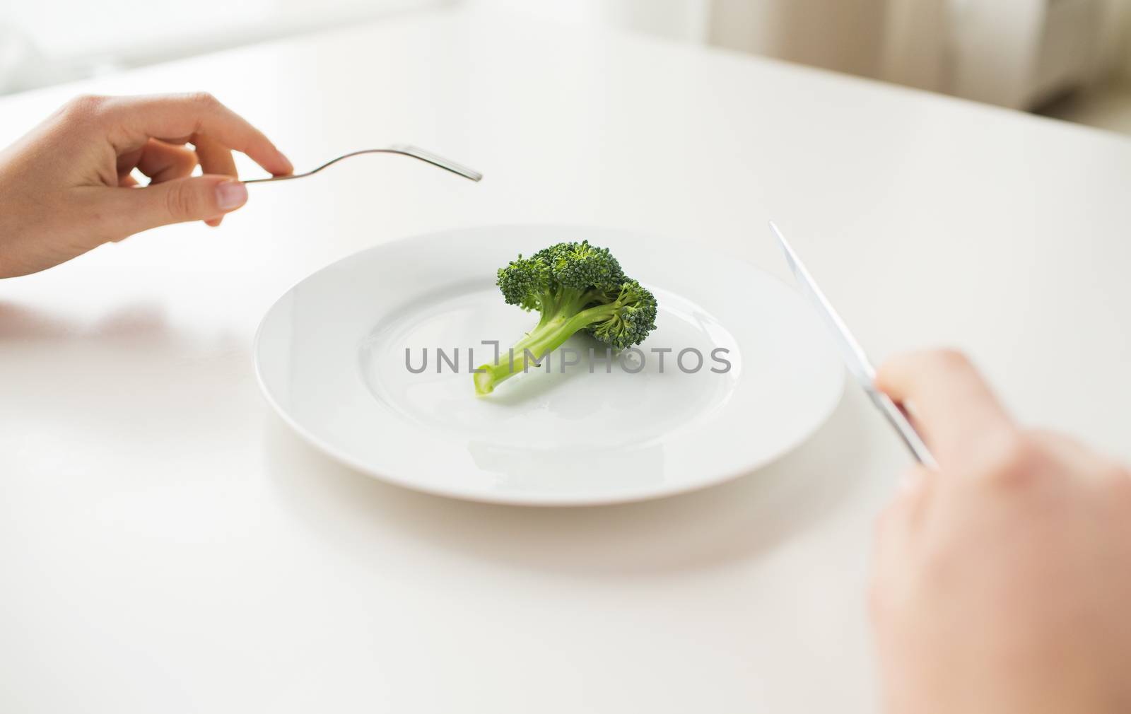 healthy lifestyle, diet, vegetarian food and people concept - close up of woman with fork and knife eating broccoli