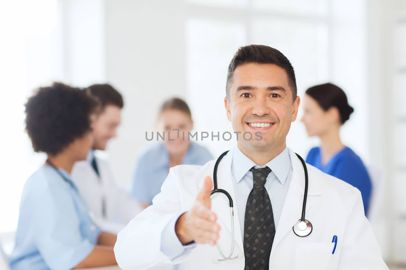 clinic, profession, people and medicine concept - happy male doctor over group of medics meeting at hospital prepared for handshake