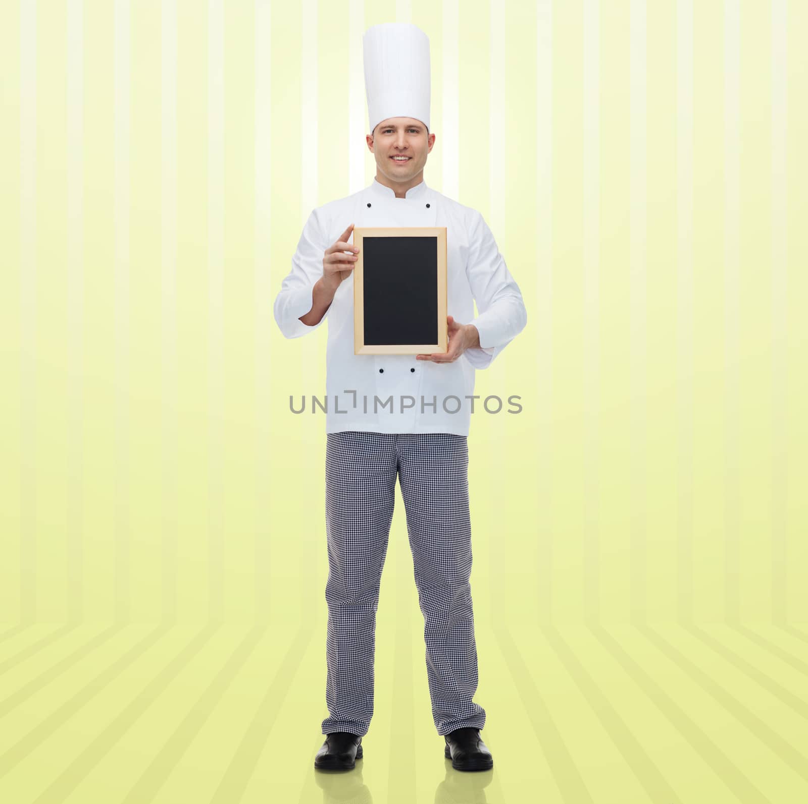 cooking, profession, advertisement and people concept - happy male chef cook showing and holding blank menu chalk board over yellow background