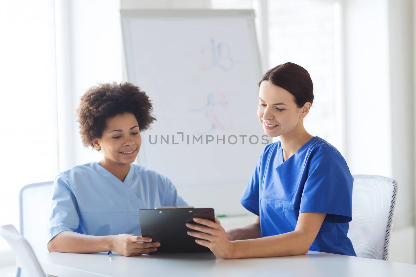 hospital, profession, people and medicine concept - group of happy doctors with tablet pc computer and clipboard meeting at medical office