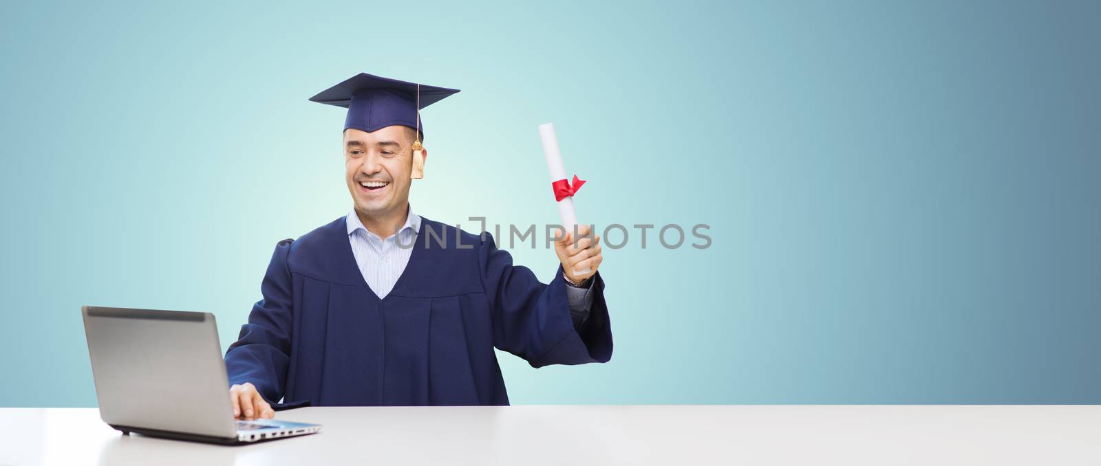 education, graduation, business, technology and people concept - happy adult student in mortarboard with diploma and laptop computer sitting at table over blue background