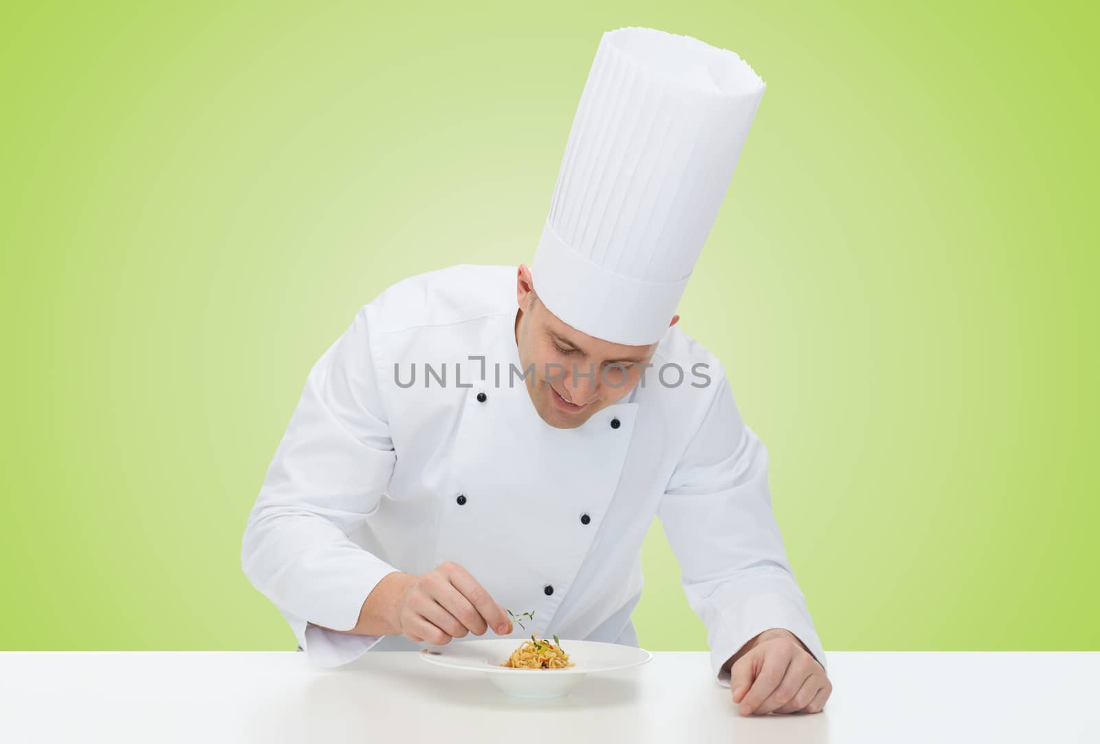 cooking, profession, haute cuisine, food and people concept - happy male chef cook decorating dish over green background