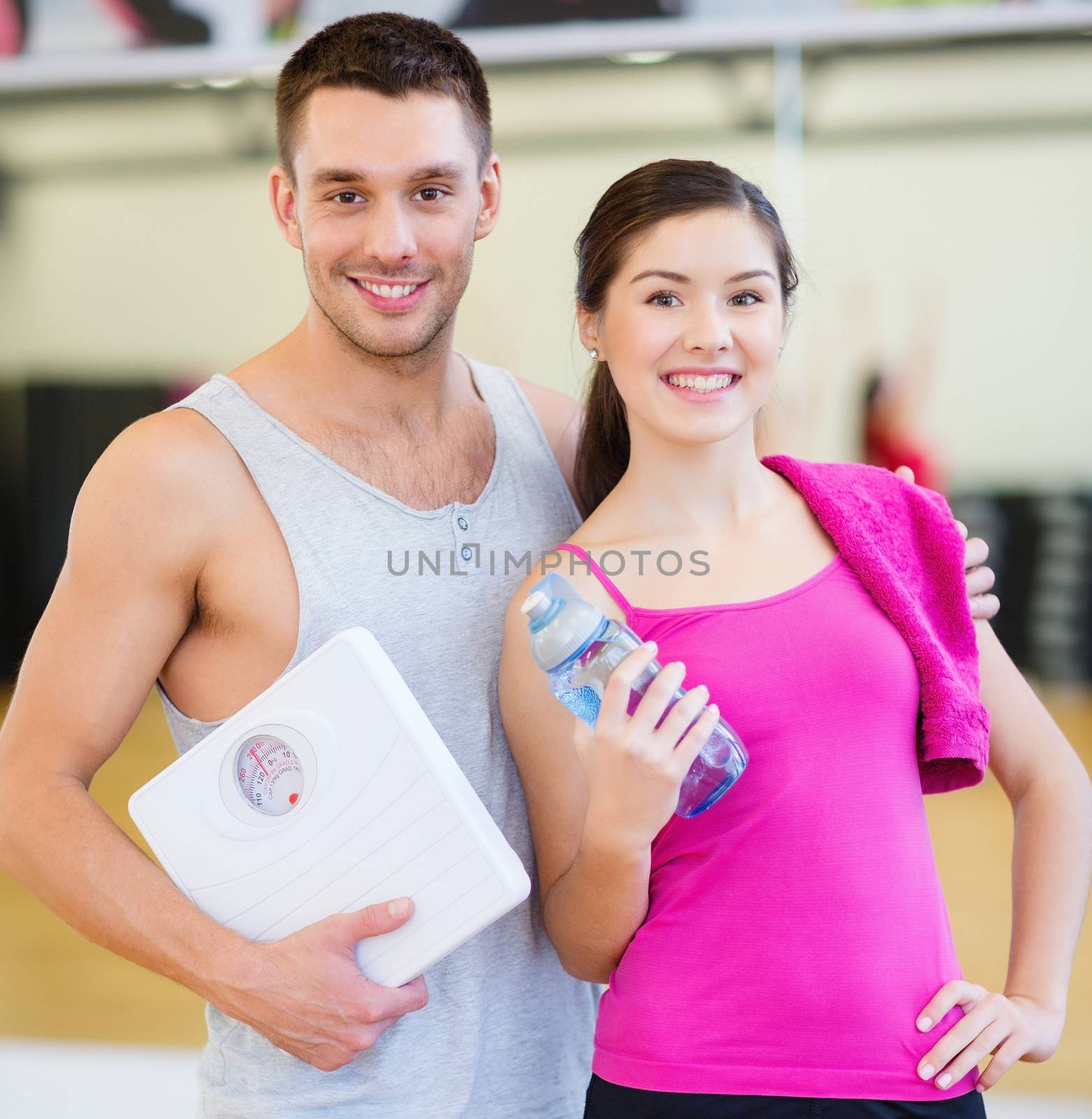 fitness, sport, training, gym and lifestyle concept - two smiling people with scale and water bottle in the gym