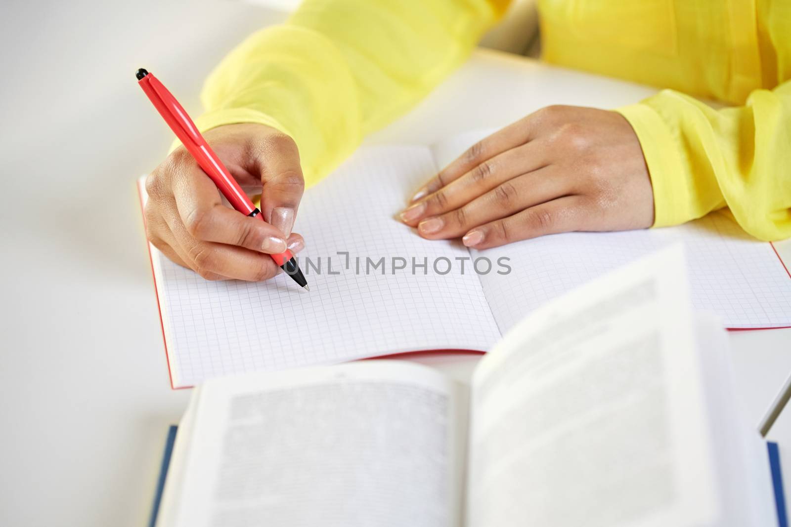 people and education concept - close up of fafrican american female hands with book writing to notebook at school