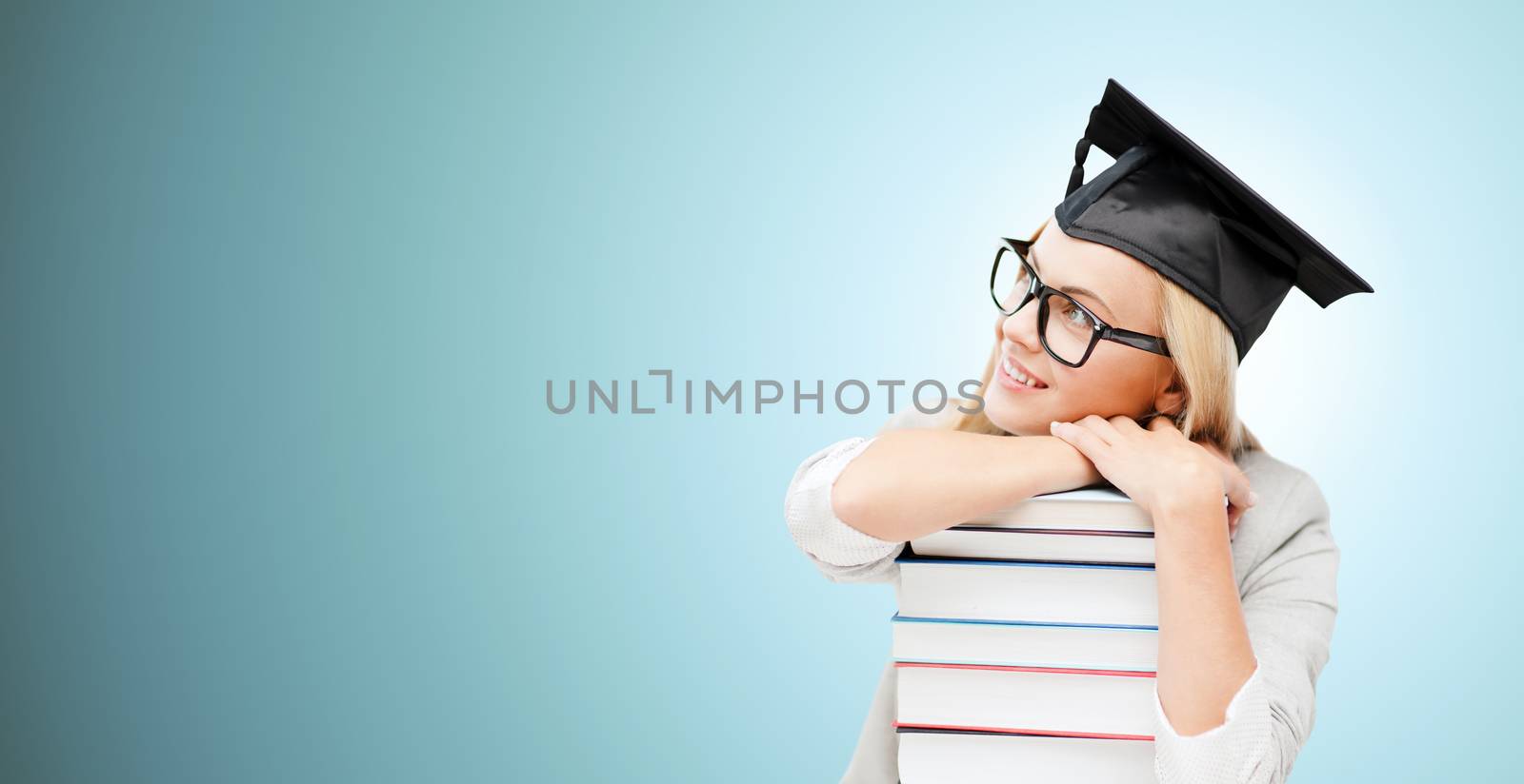 education, happiness, graduation and people concept - picture of happy student in mortar board cap with stack of books daydreaming over blue background
