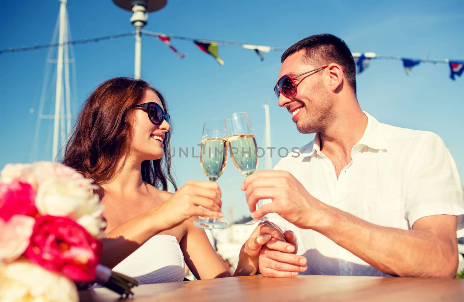 love, dating, people and holidays concept - smiling couple wearing sunglasses drinking champagne and looking to each other at cafe