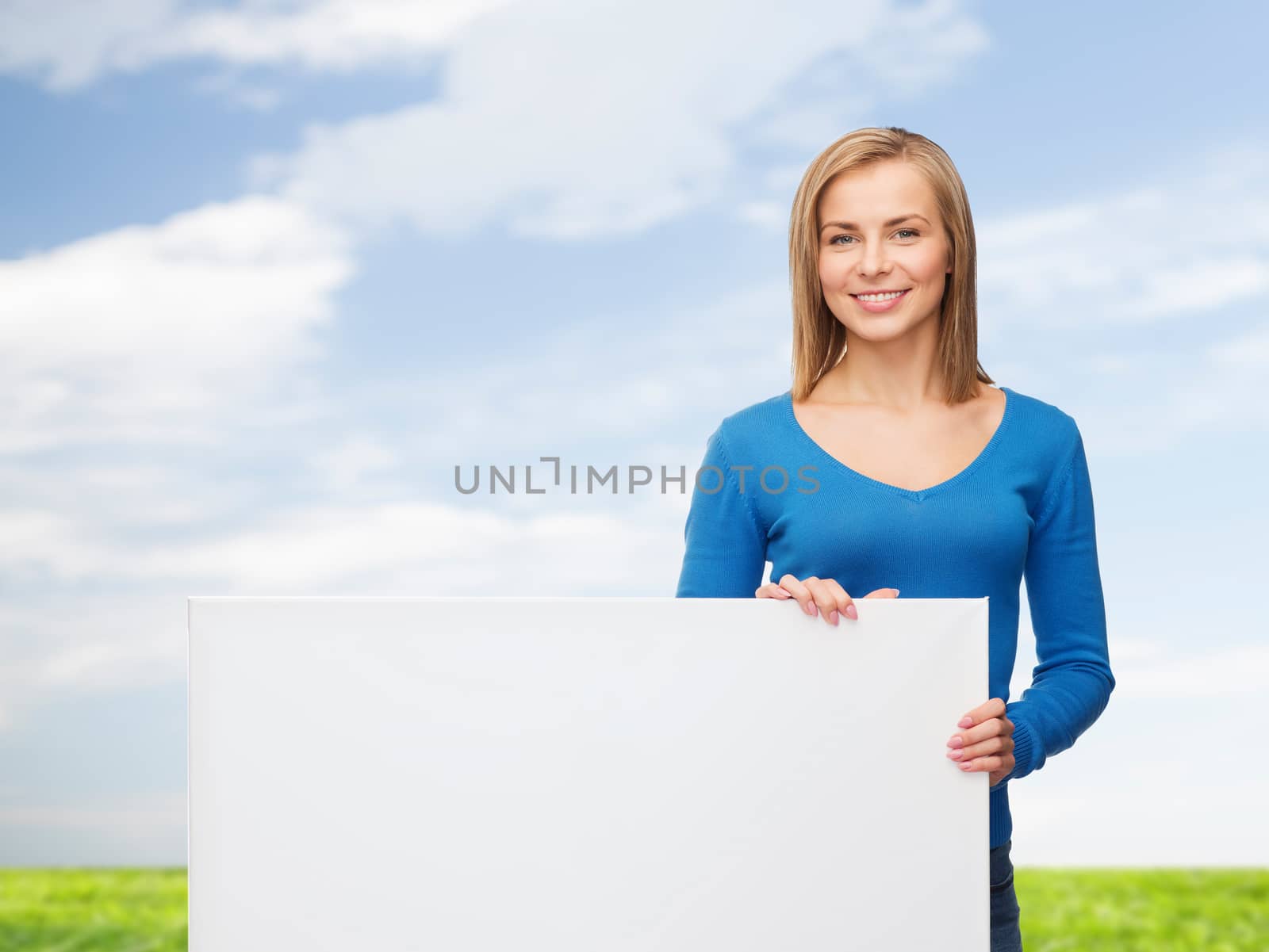 people, advertisement and sale concept - smiling young woman with blank white board over blue sky and grass background
