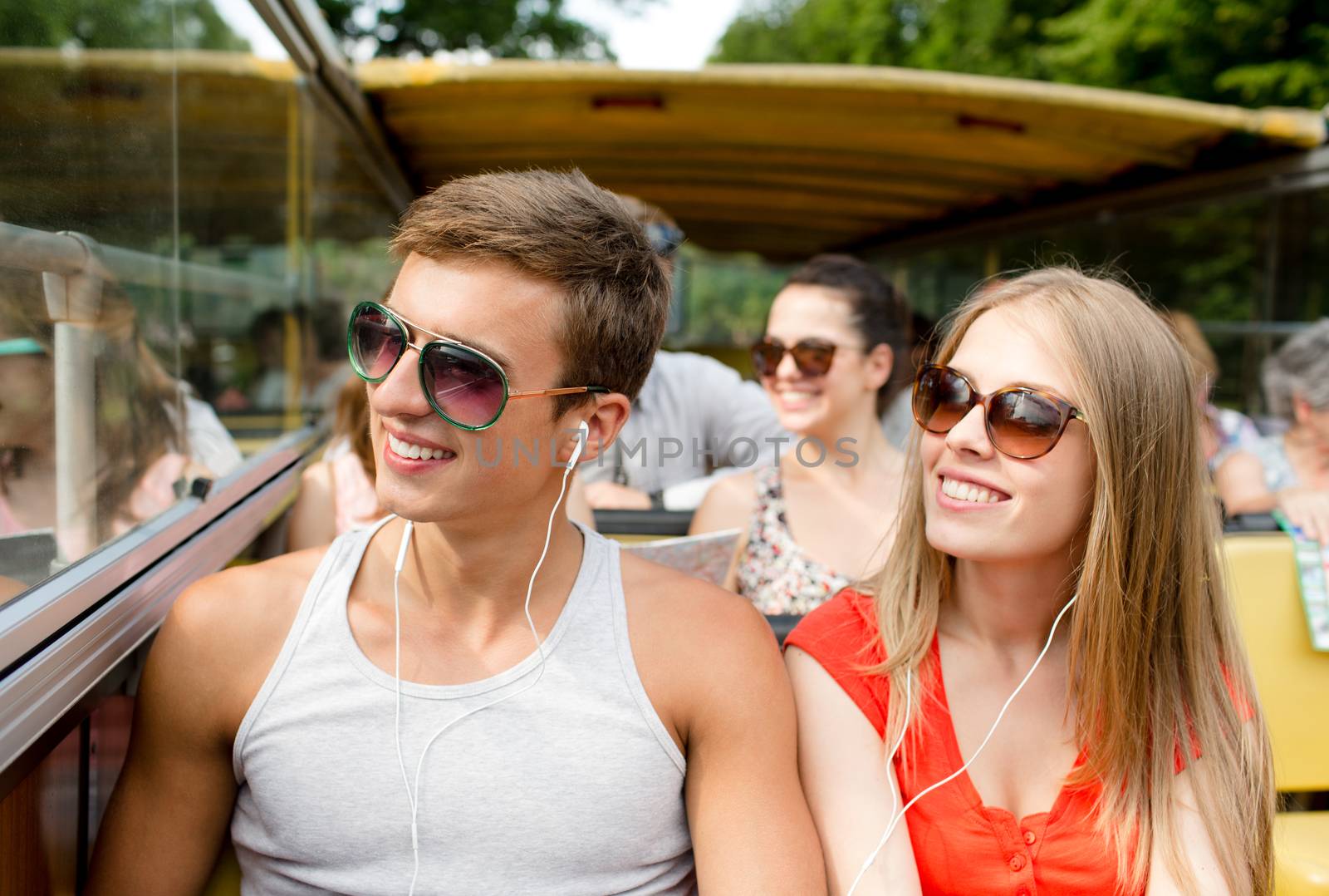friendship, travel, vacation, summer and people concept - smiling couple with earphones traveling by tour bus