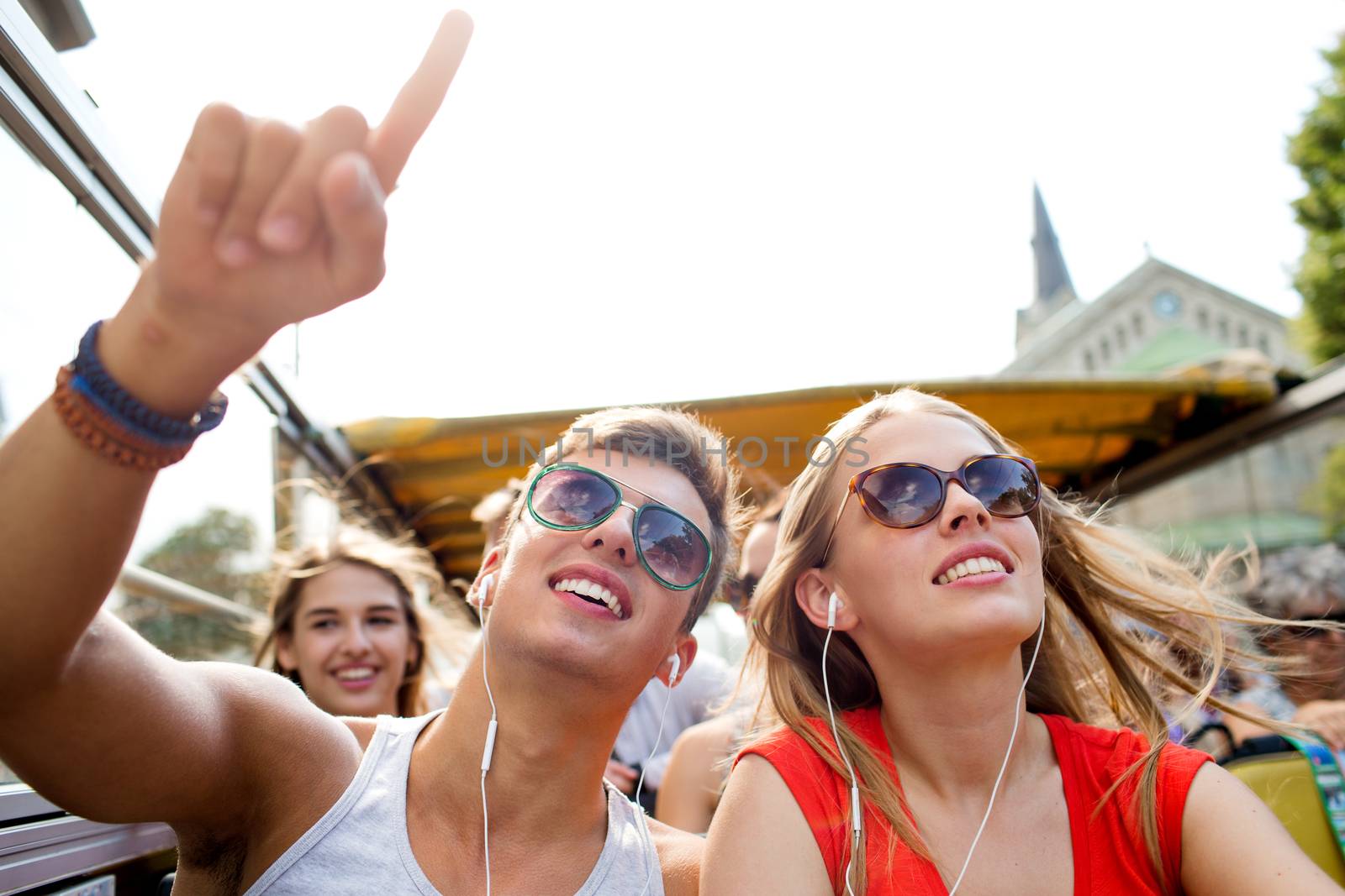 friendship, travel, vacation, summer and people concept - smiling couple with earphones traveling by tour bus and pointing finger