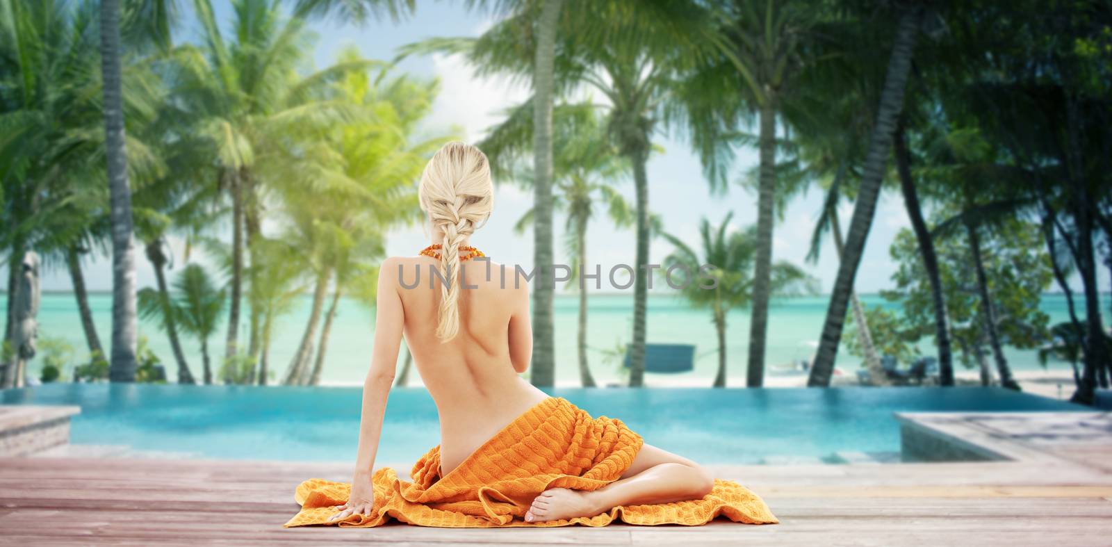 people, travel, tourism, summer and people concept - woman with orange towel from back over tropical beach with swimming pool background