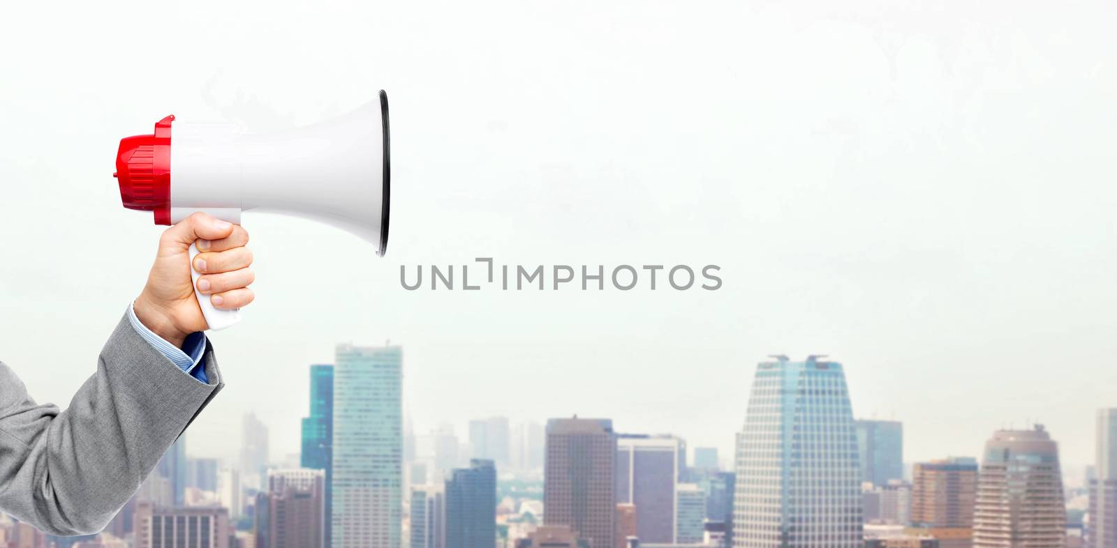 business, people and public announcement concept - close up of male hand in suit with megaphone over city background